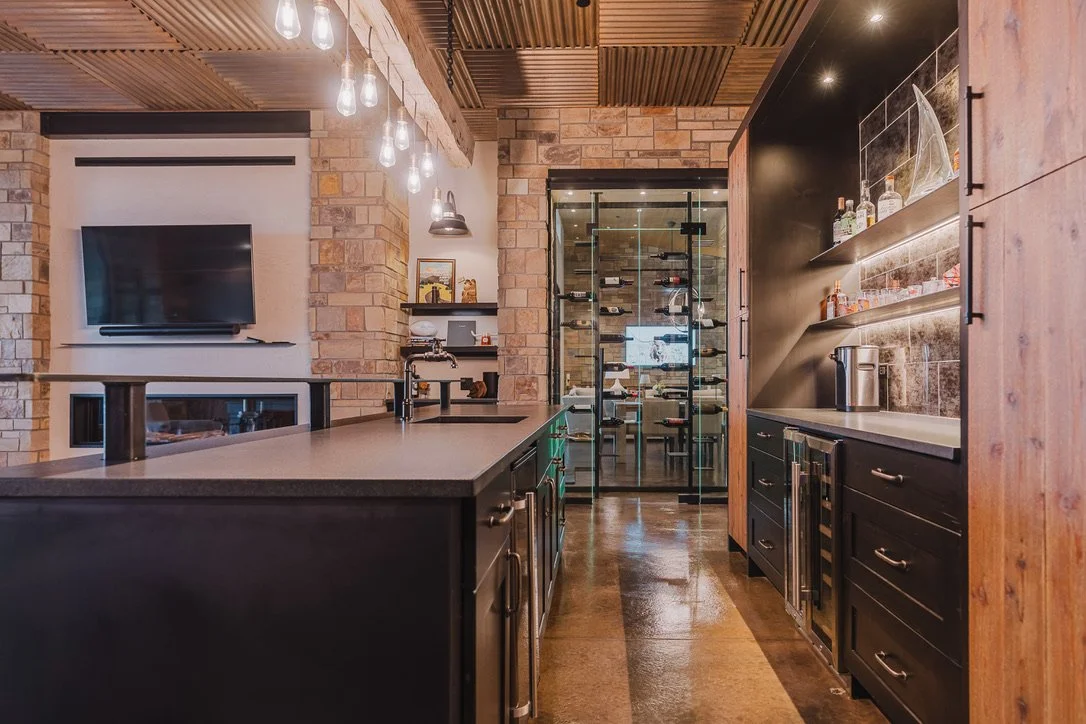 Modern kitchen with exposed wood beams, black cabinetry, stone walls, a glass wine cellar, and contemporary lighting fixtures.