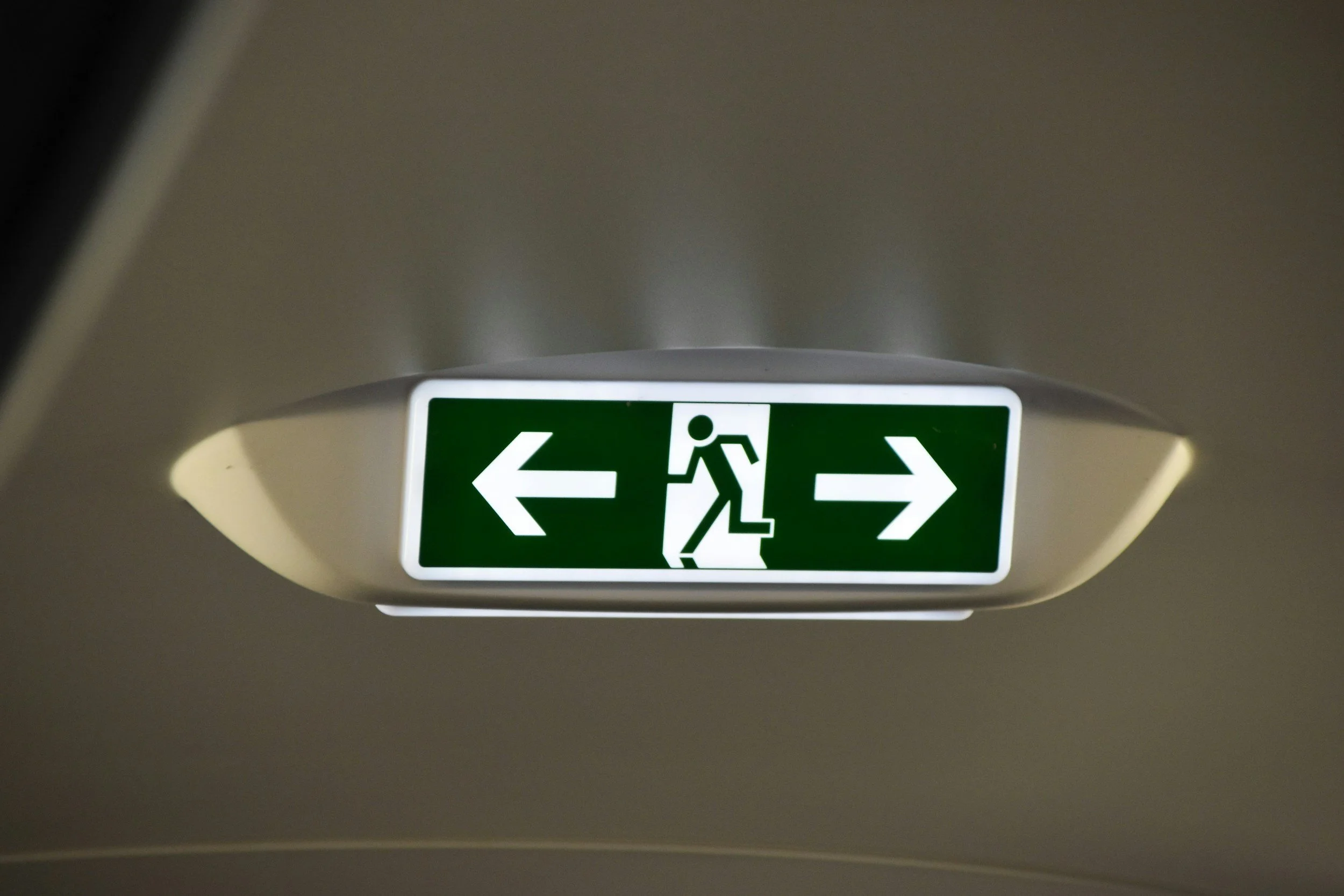 Emergency exit sign with a figure running through a door, arrows pointing left and right.