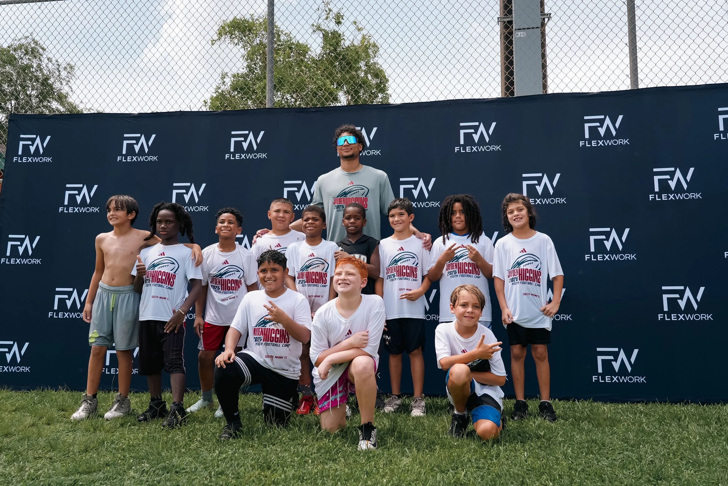 Group of children and a coach posing outdoors in front of a black backdrop with white