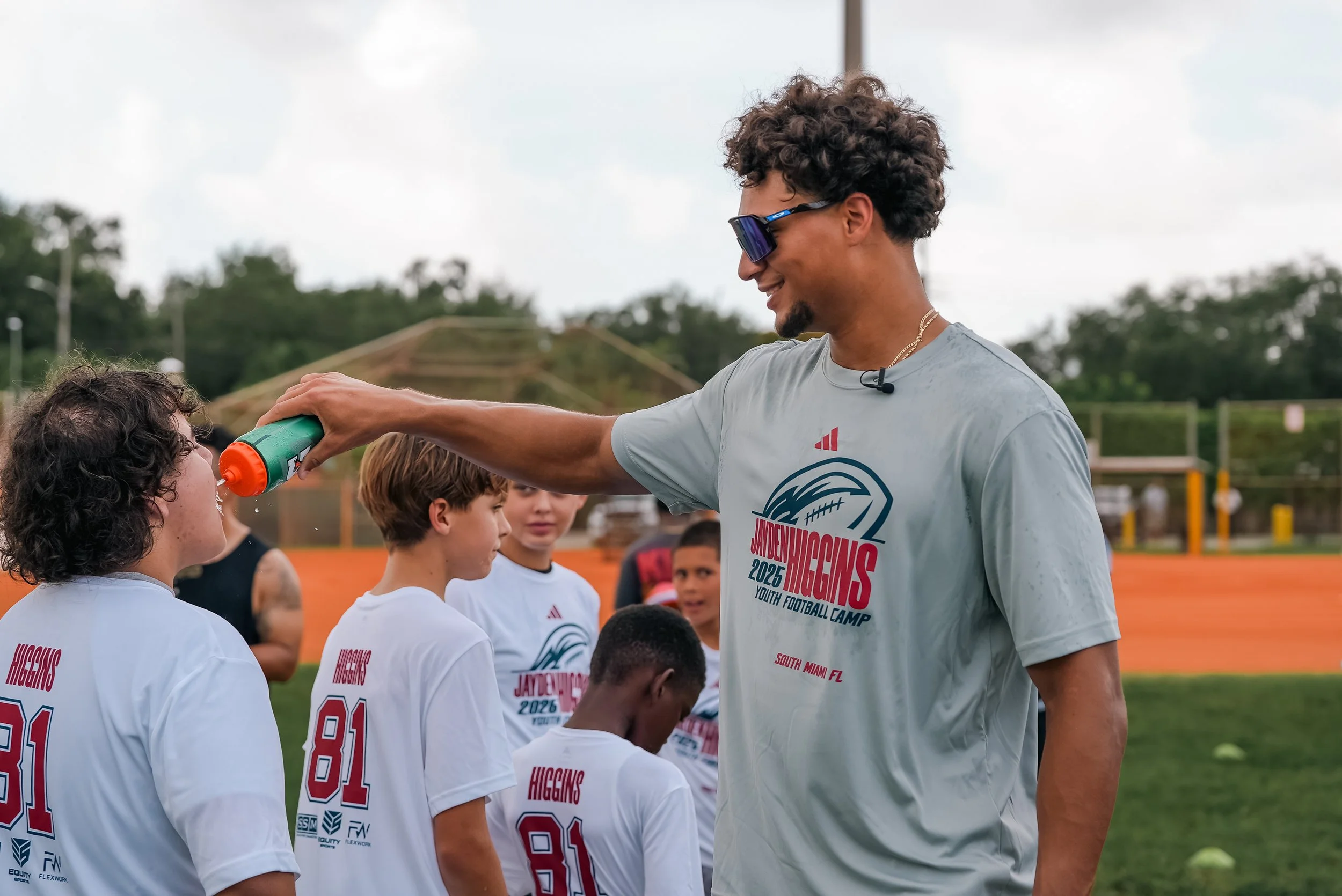 A coach cools down young football players with water spray during a practice session on a football field.