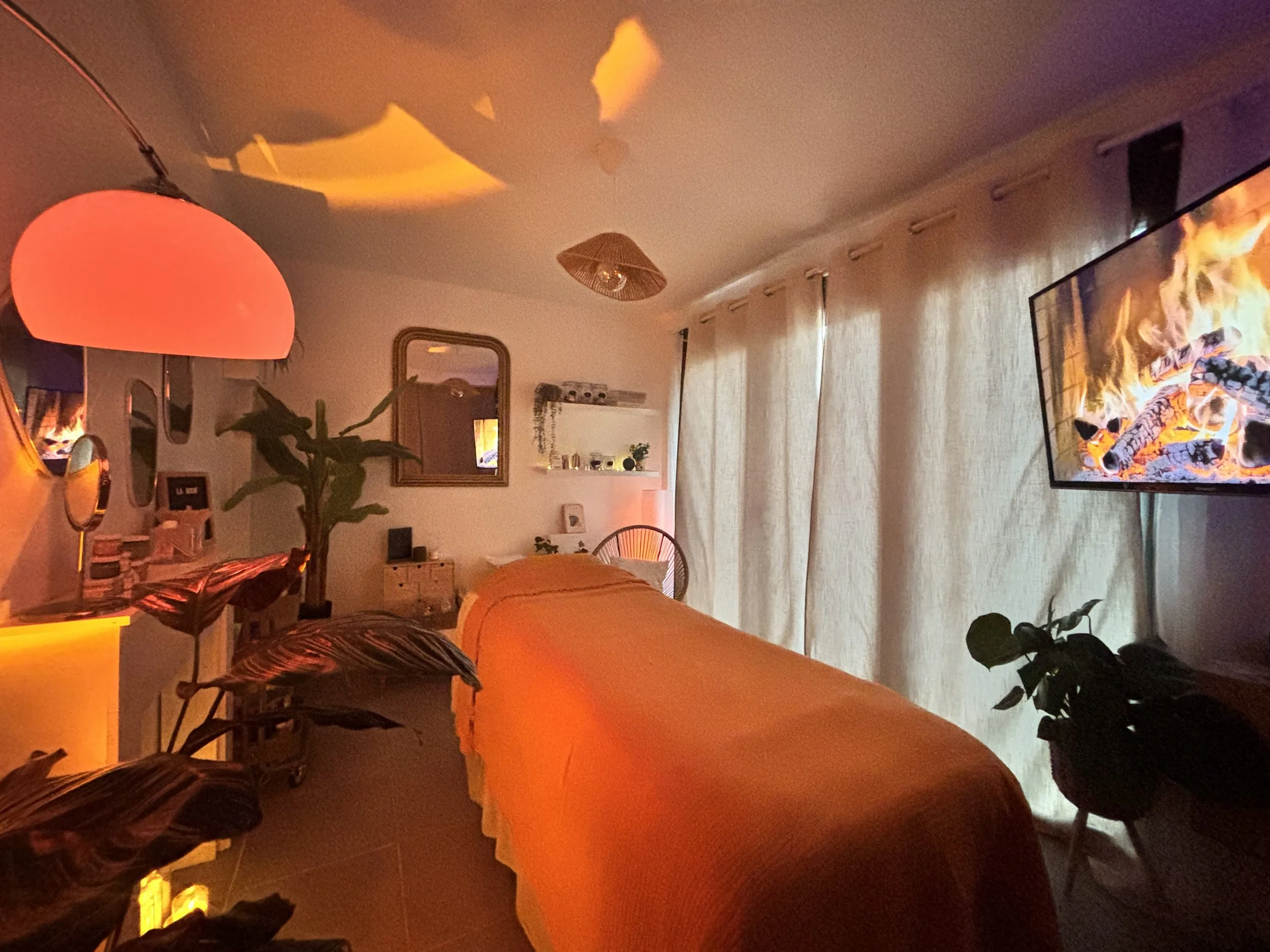 Une chambre chaleureuse avec un lit orange, une grande télévision, plusieurs lampes d'ambiance et des plantes d'intérieur, le tout sous un éclairage doux coloré.