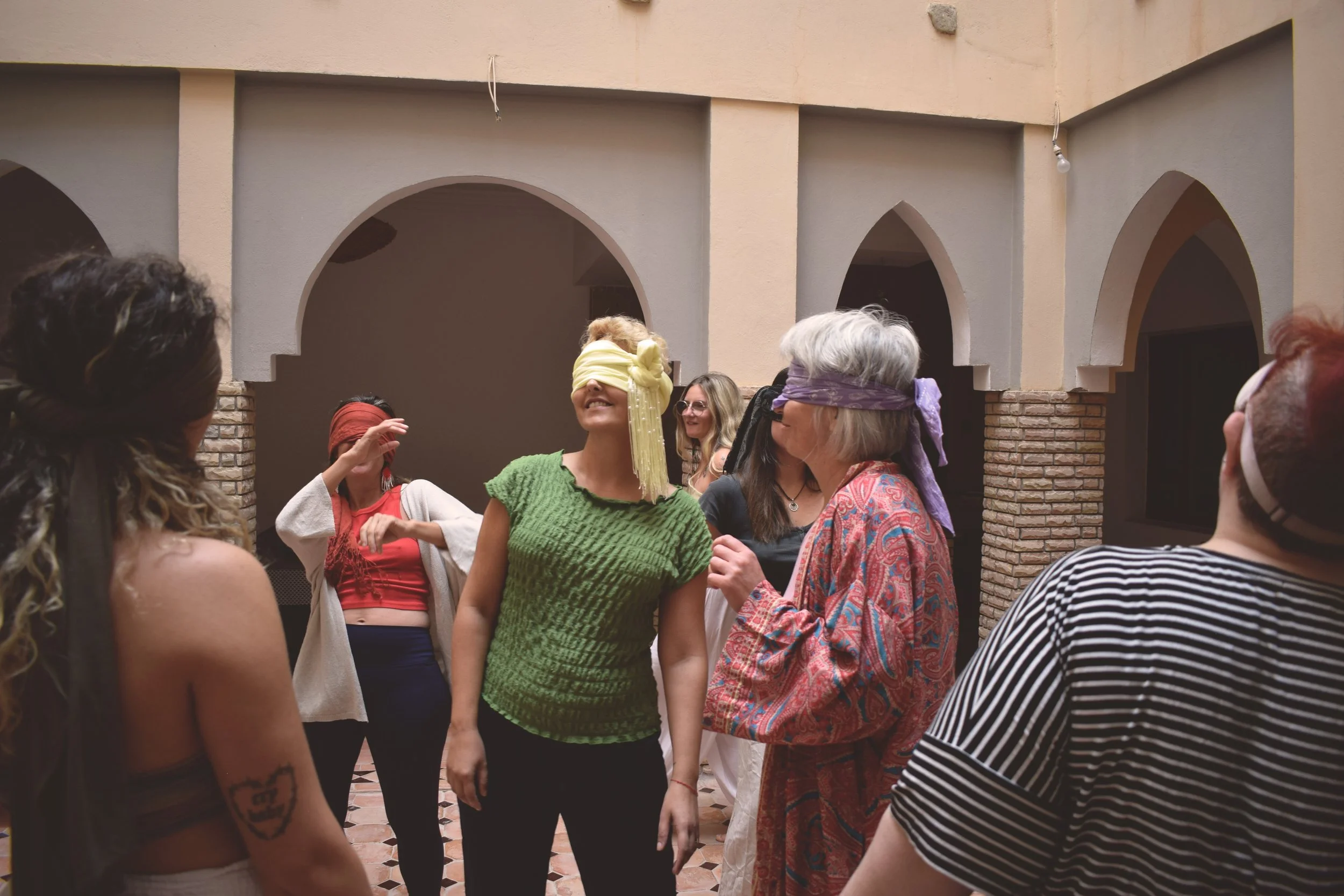 Group of women participating in a sensory activity with blindfolds in a room with arches and brick walls.