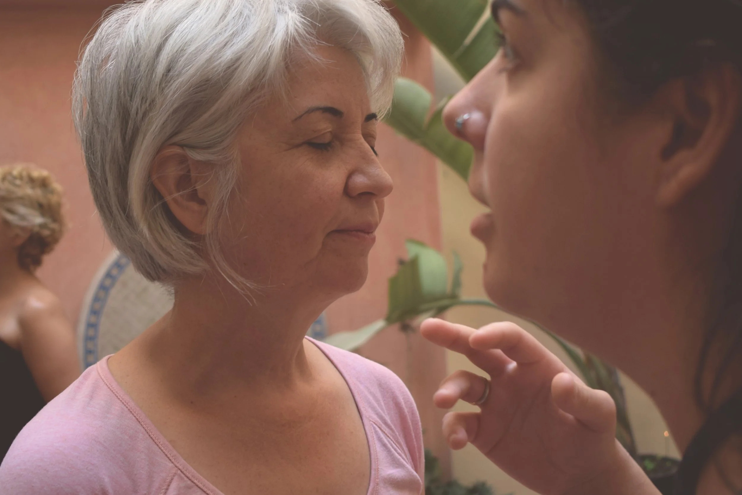 A close-up of two women, one with gray hair and light skin, and the other with dark hair and slightly darker skin, face to face with eyes closed, seemingly about to kiss or share a tender moment.