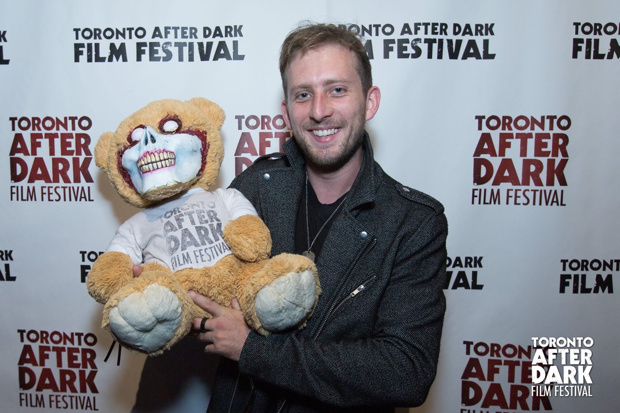 A smiling man holding a teddy bear with a painted skull face at the Toronto After Dark Film Festival.