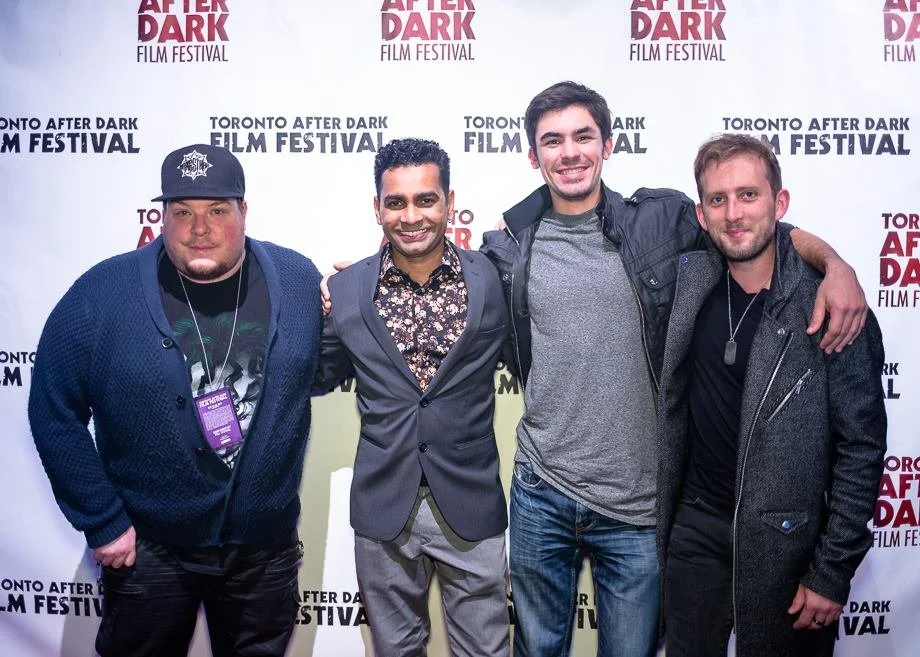 Four men smiling and standing arm-in-arm in front of a backdrop with the text 'Toronto After Dark Film Festival'.