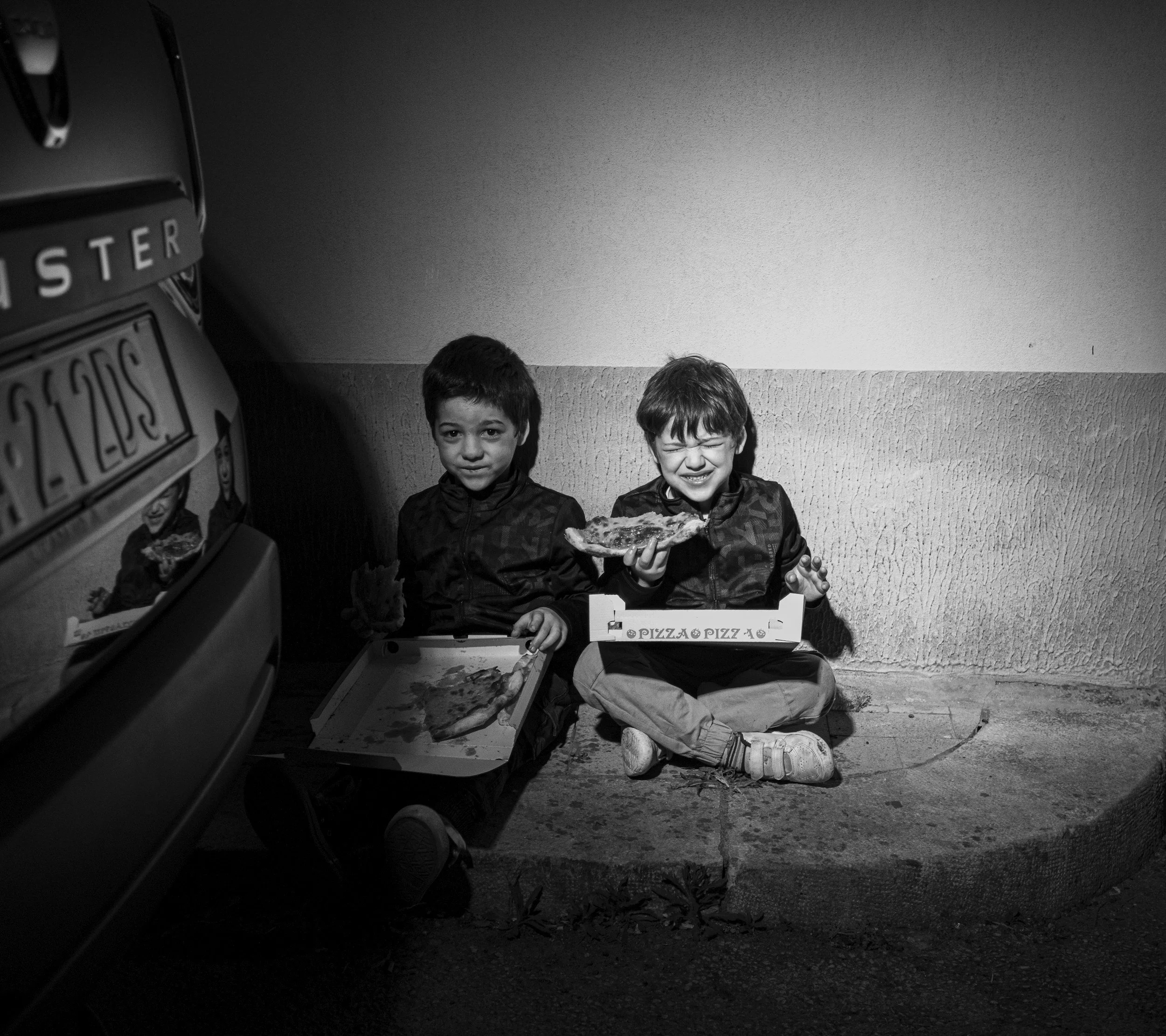 Two young boys sitting on the ground sharing a pizza. mārinate. tells human stories through the lens of food.