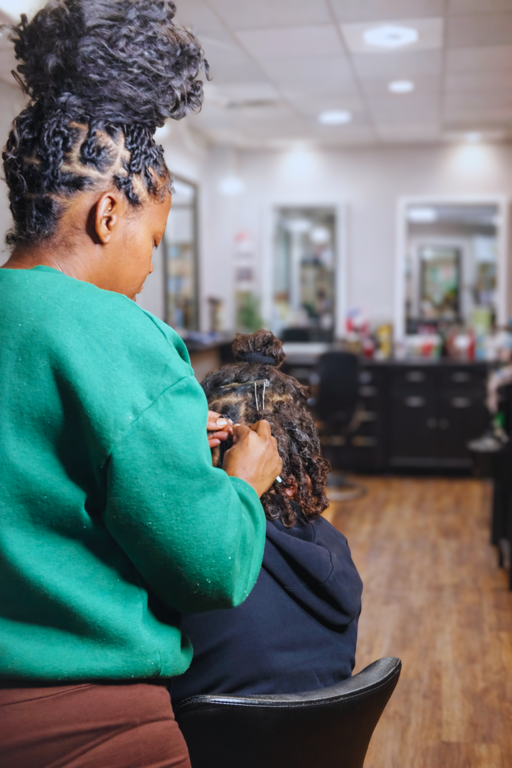 A hairstylist working on a client's curly hair in a salon, with mirrors and salon equipment in the background.