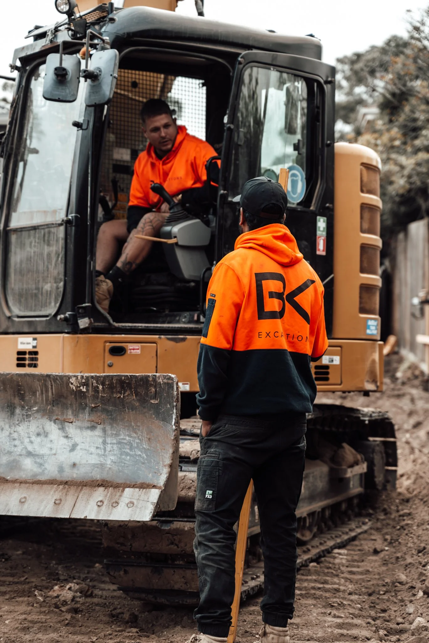 Two construction workers wearing orange safety jackets with