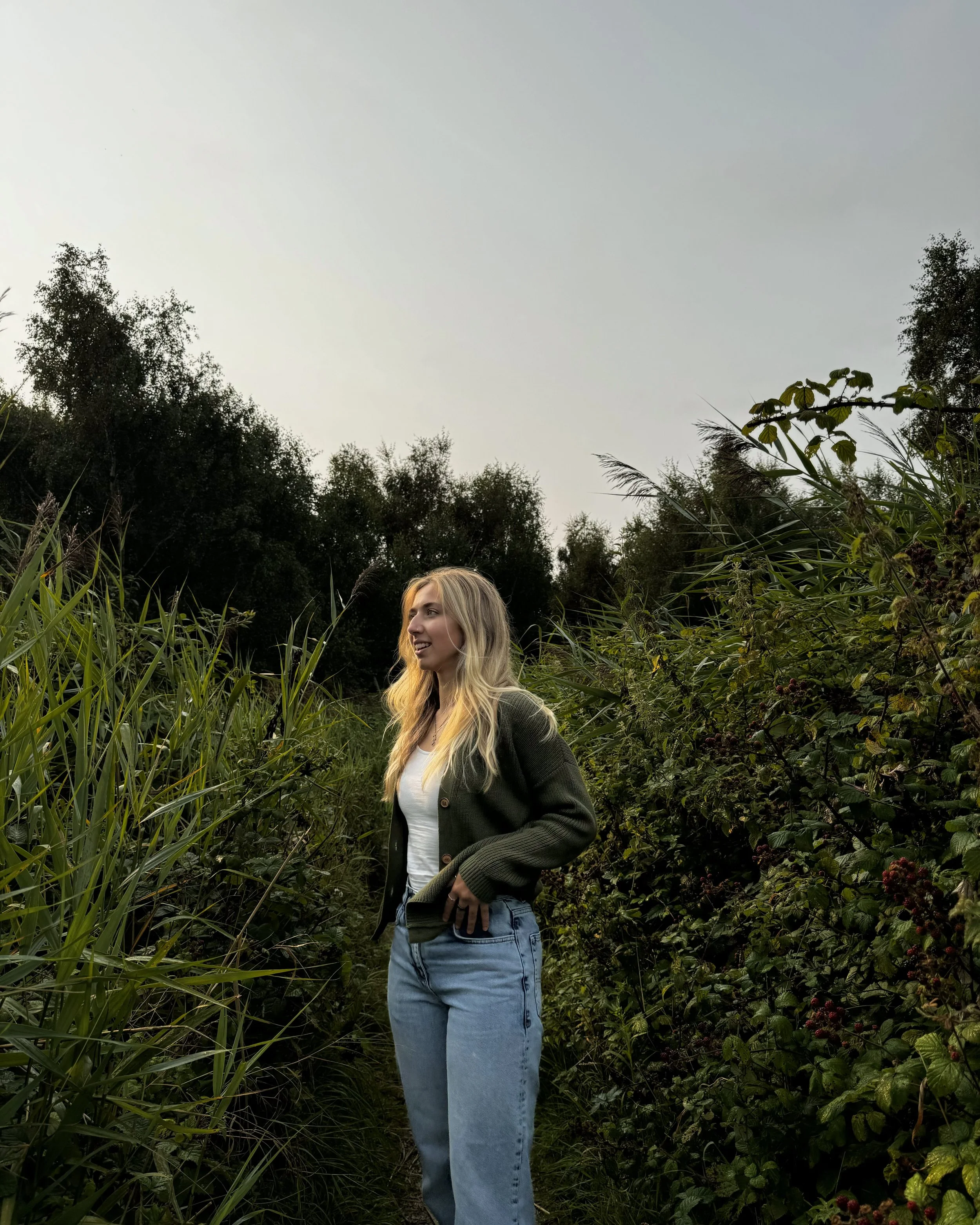 A photo of a woman stood in greenery and leaves.