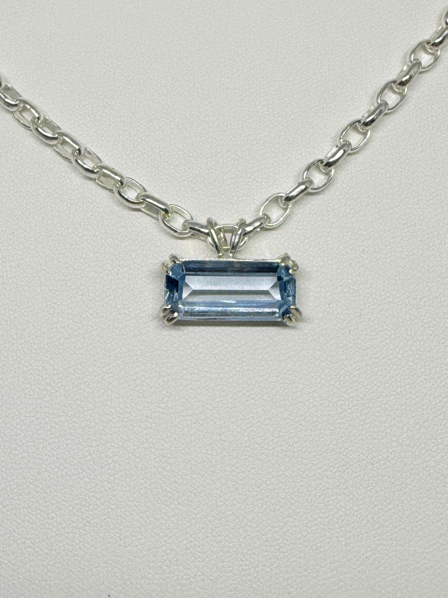 A silver chain necklace with a rectangular blue gemstone pendant, resting on a plain white background.