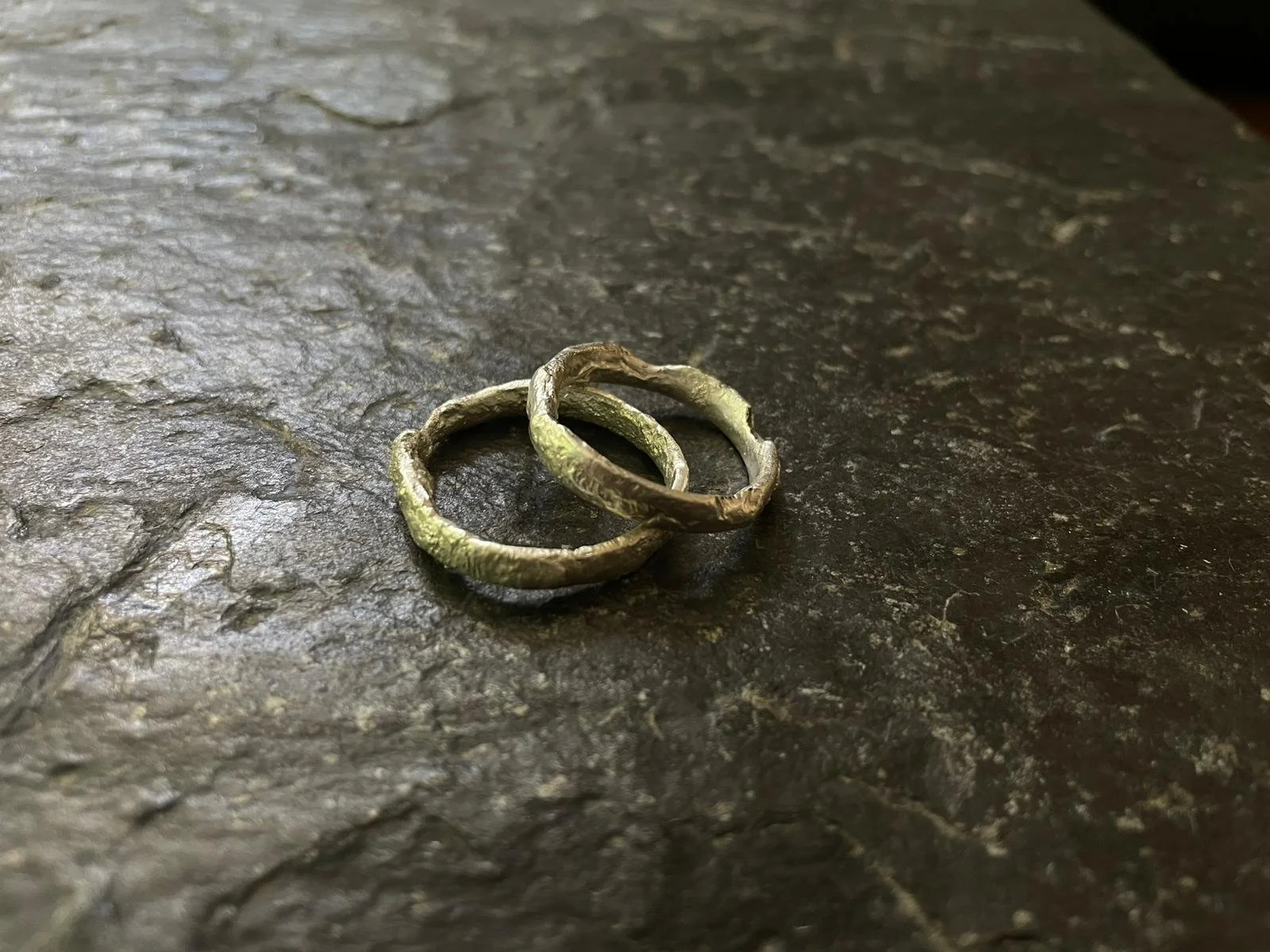 Two silver rings with a textured surface on a dark, rough stone surface.