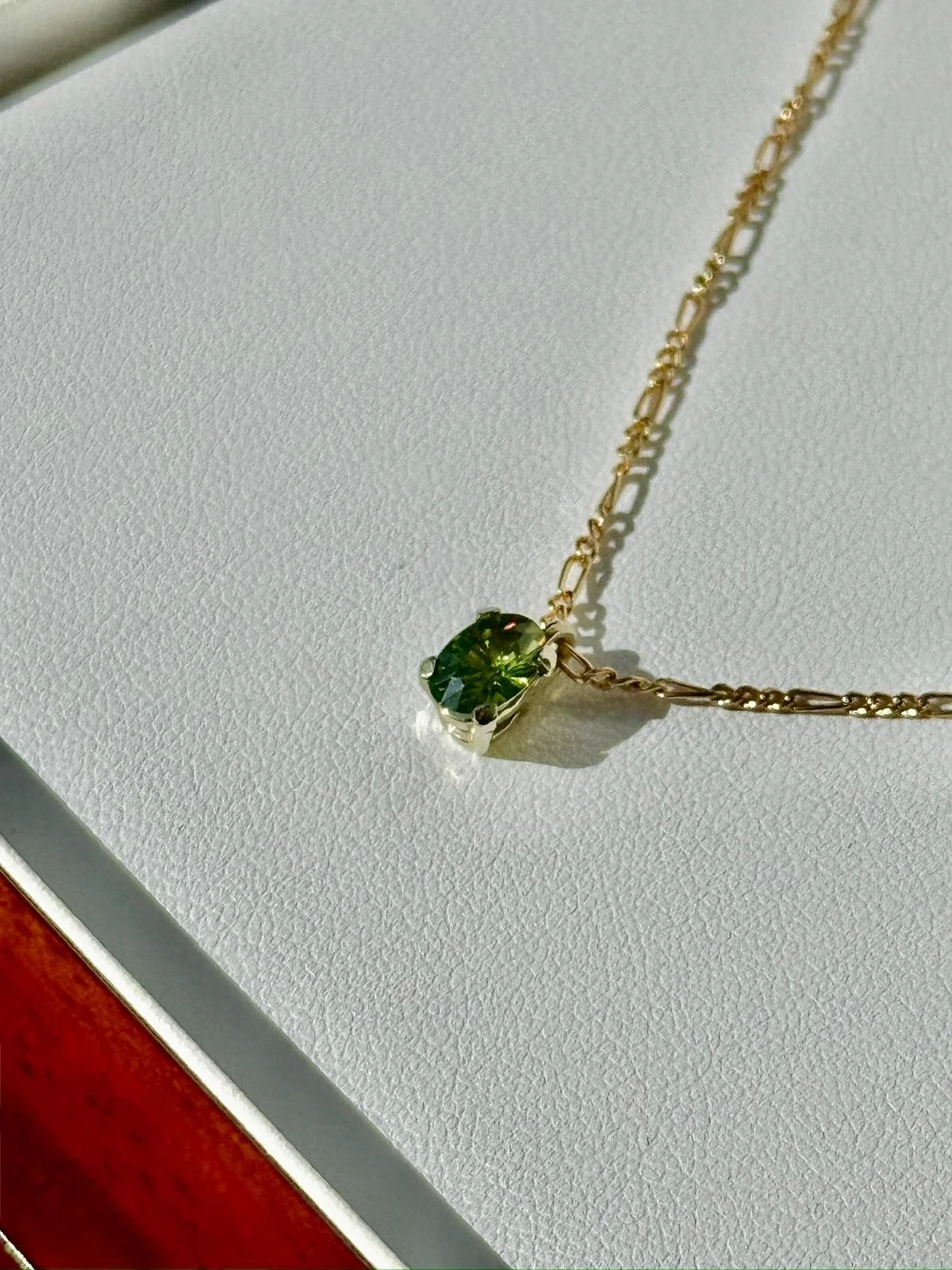A gold chain necklace with a green gemstone pendant on a white textured surface.