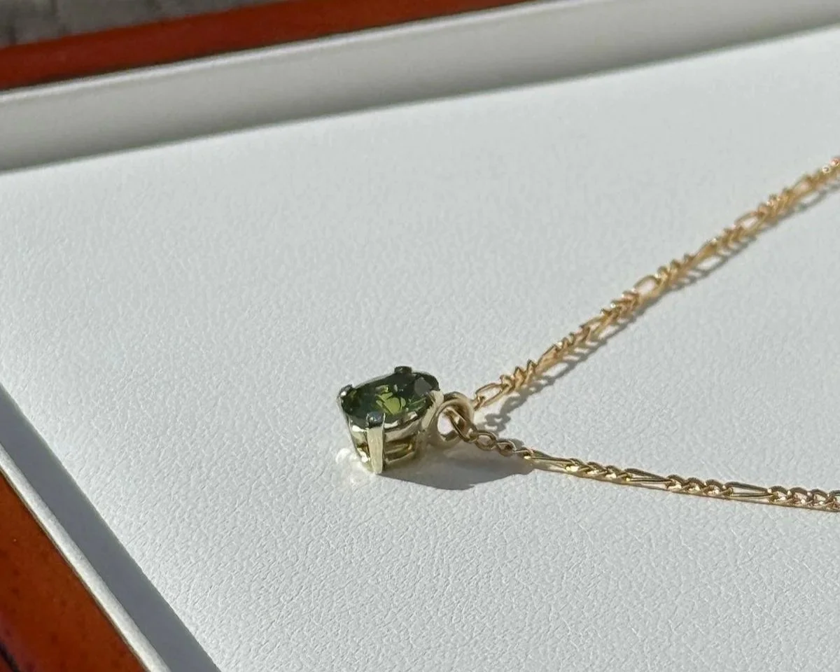 Gold chain necklace with a dark green gemstone pendant on white background.