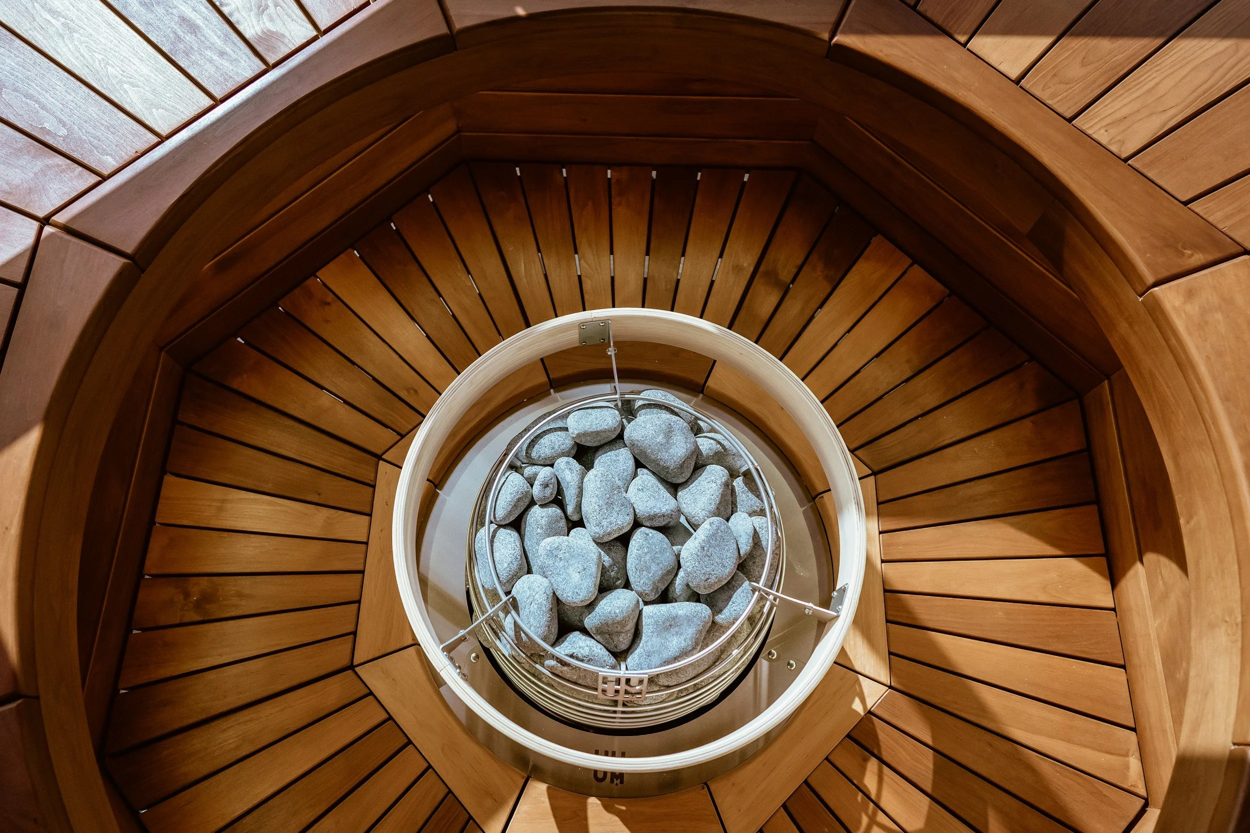 View from above of a wooden sauna with a container of grey stones at the center.