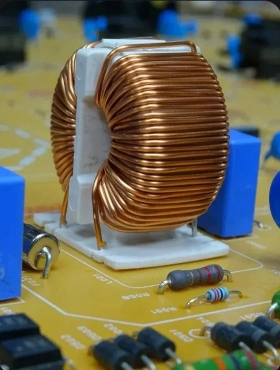 Close-up of a large copper coil on a circuit board with resistors and blue components visible.