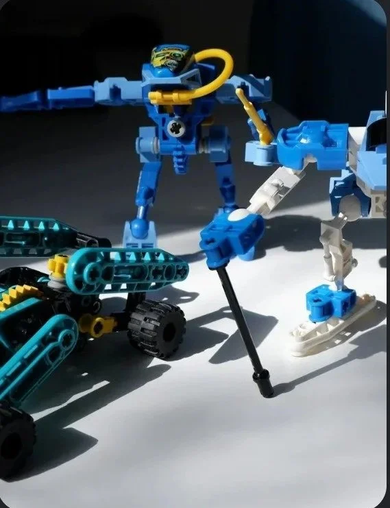 LEGO robotic creatures and vehicles on a white surface with shadows, including a blue and yellow robot, a blue and white animal figure, and a vehicle with black wheels.