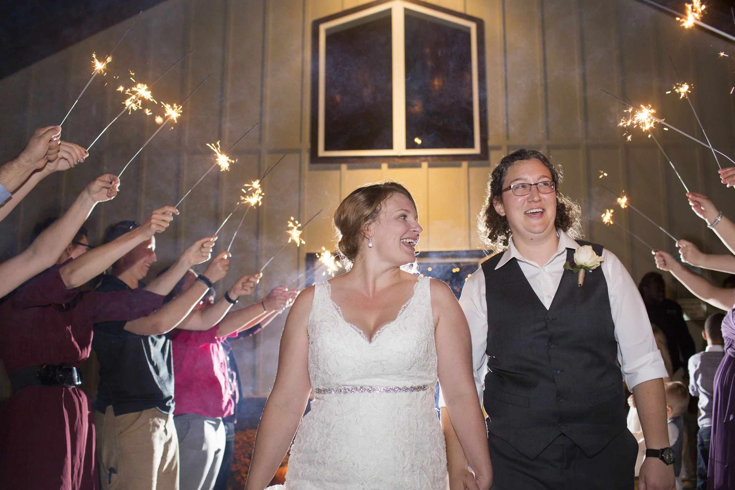 A newlywed same-sex couple celebrating their wedding surrounded by friends holding sparklers for their wedding exit at Sable and Vine formerly The Barn at Vino