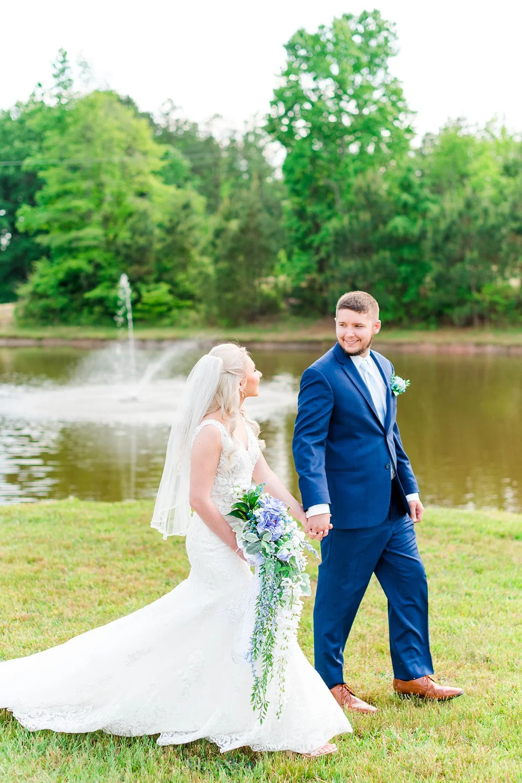 A bride and groom walk hand in hand outdoors near the sable and vine outdoor water fountain in their spring wedding