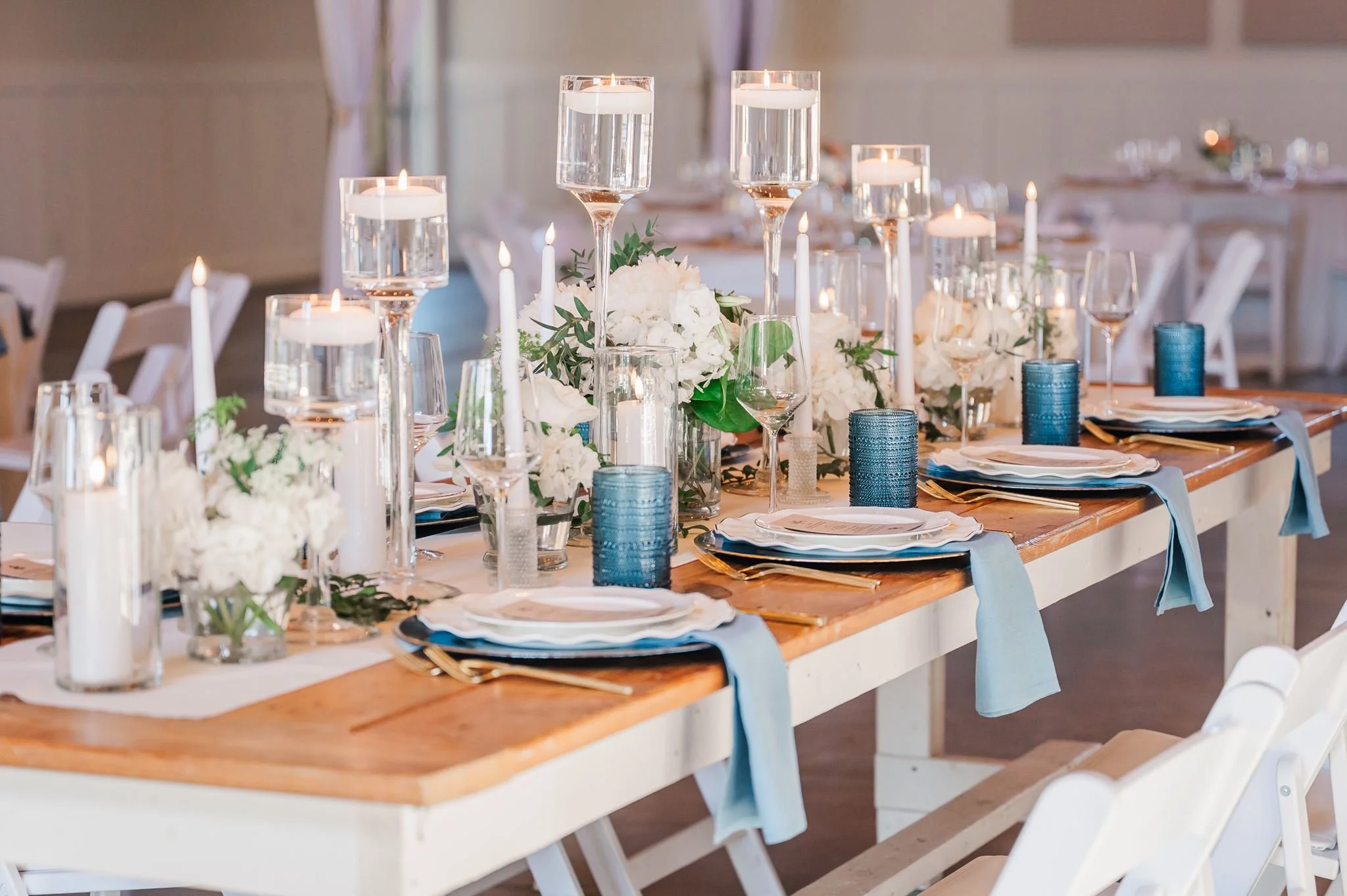 Elegant dining table setup with white floral centerpieces, candles, and glassware for a formal event.