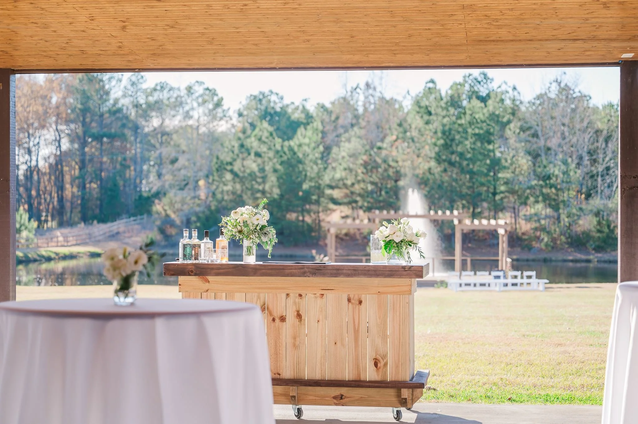 Outdoor patio with a mobile bar with the pergola and water fountain altar backdrop at Sable & Vine, an event venue in Stem, North Carolina