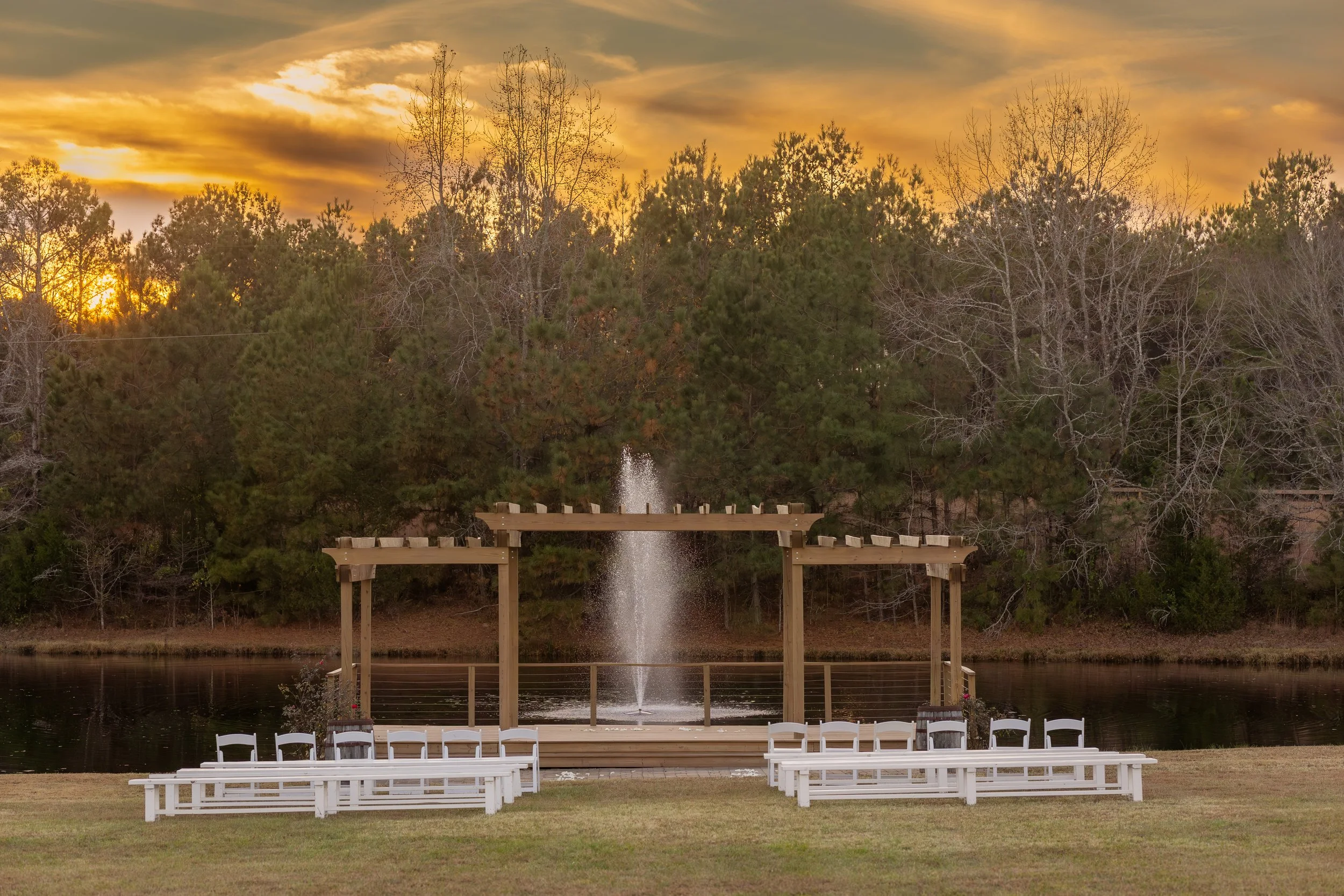 Our pergola event space surrounded by trees with a sunset in the background with in-house seating rentals for your wedding ceremony at our Granville County NC wedding venue