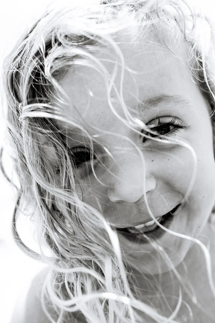 Close-up black and white photo of a smiling woman with wet, curly hair partially covering her face.