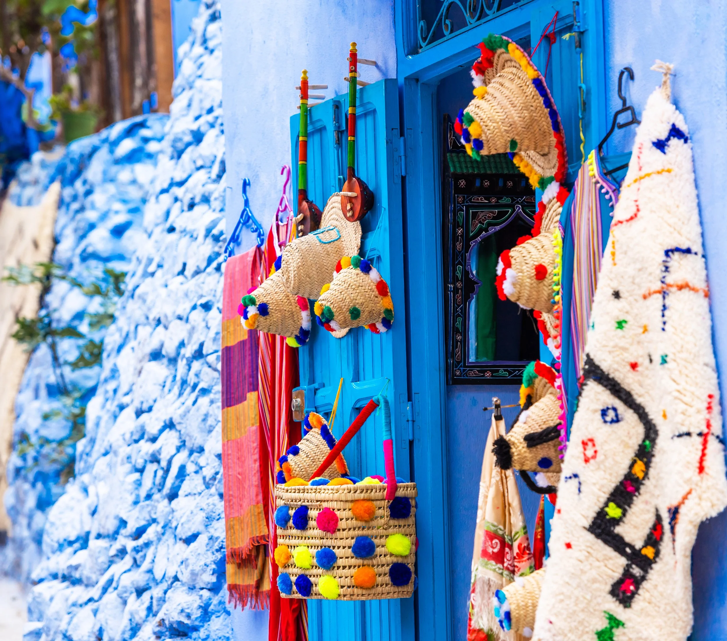 Colorful accessories and textiles hanging outside a bright blue door of a building with a textured white wall.