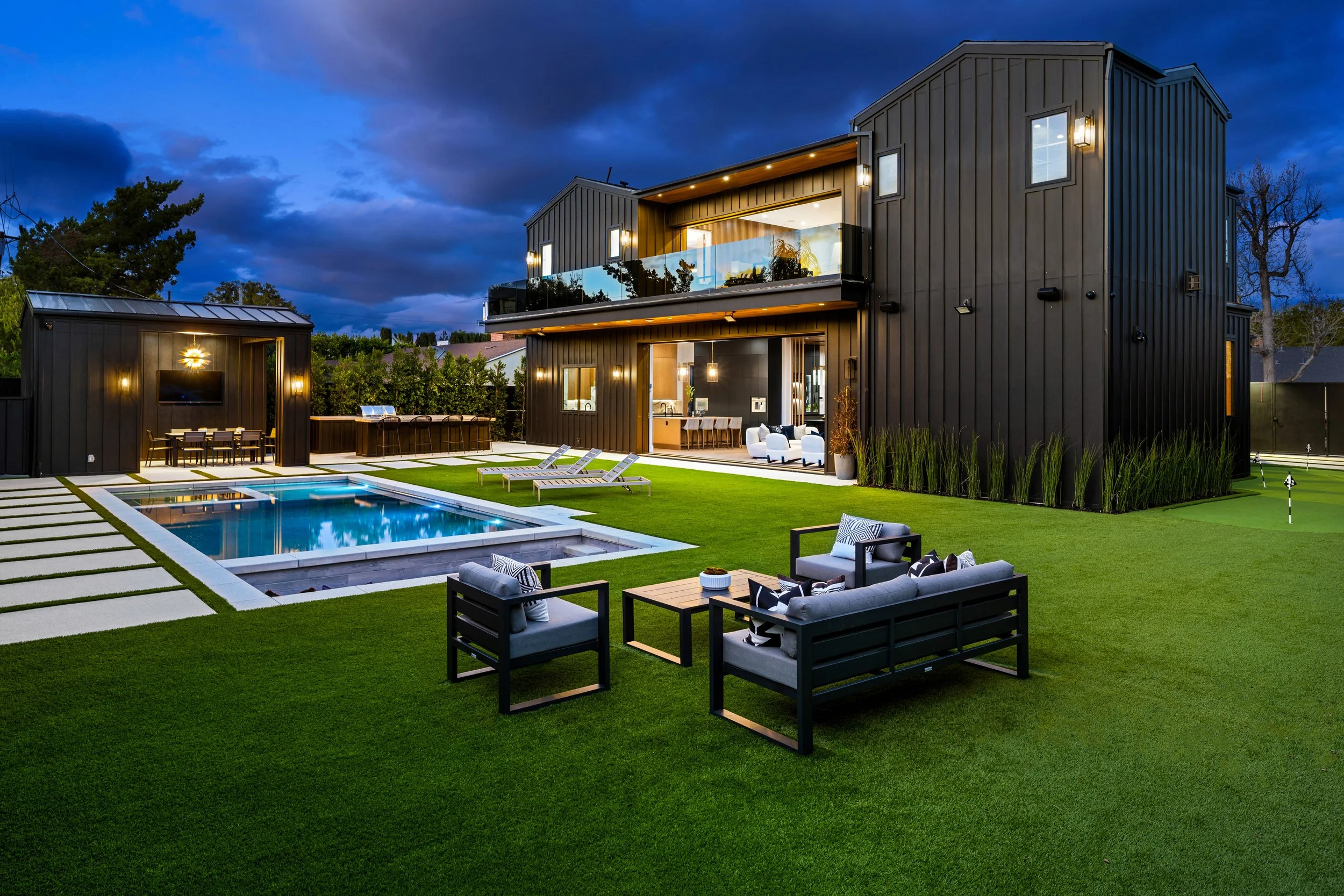 Modern black two-story house with outdoor pool and patio furniture at dusk
