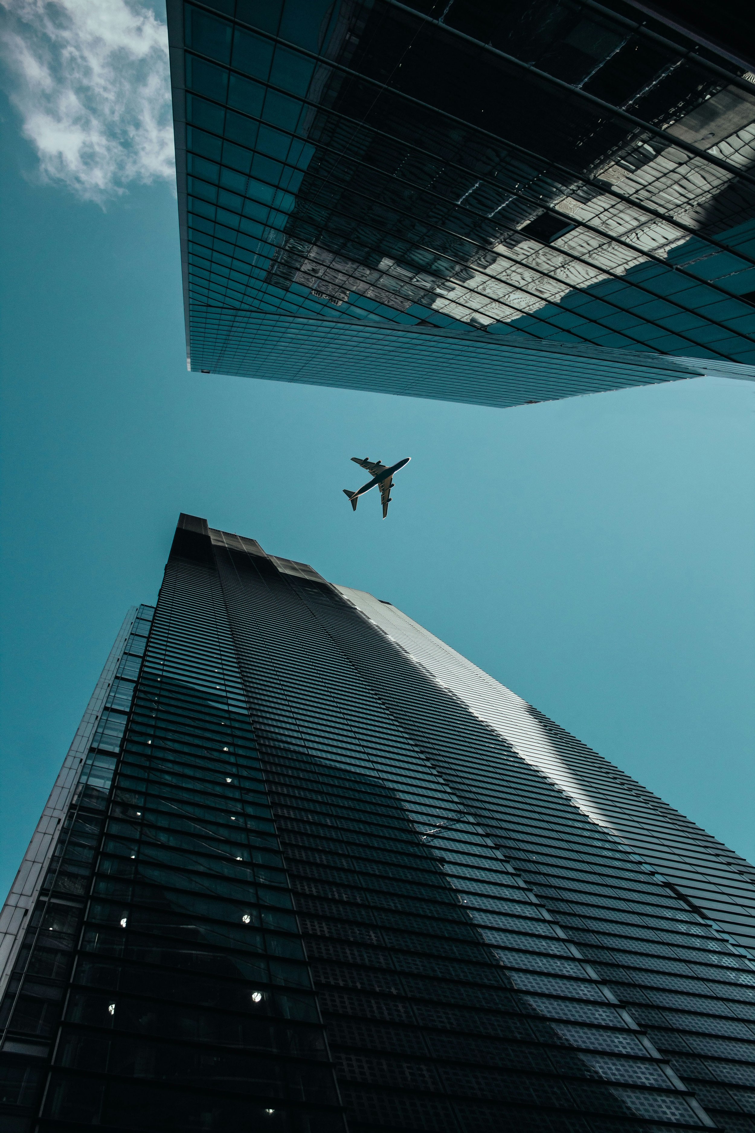 Looking up at a modern skyscraper with reflective glass windows and an airplane flying overhead against a blue sky with clouds.