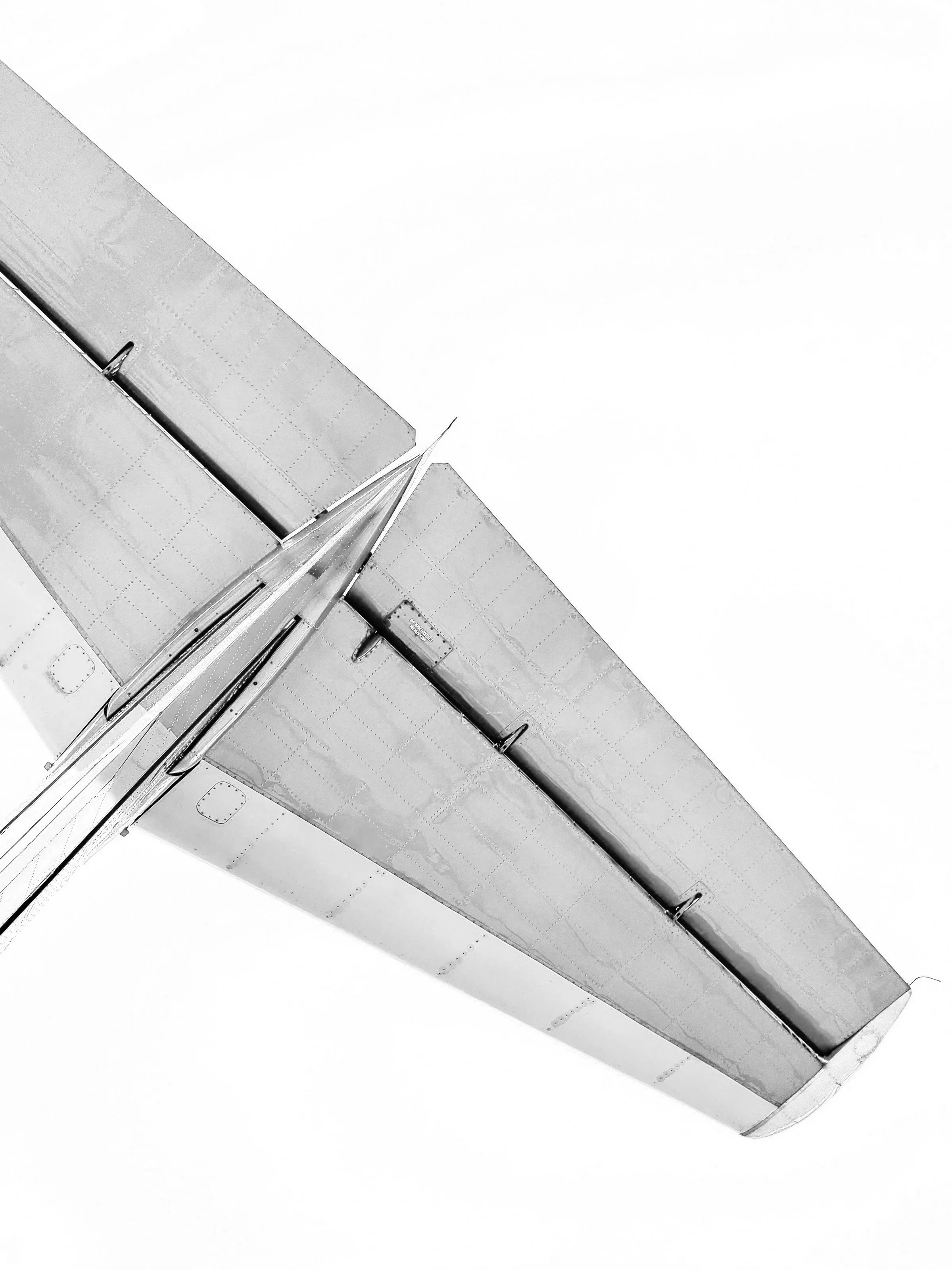 Close-up of the wing of a large airplane, showing metallic surface with rivets and structural details, viewed from below against a pale sky.