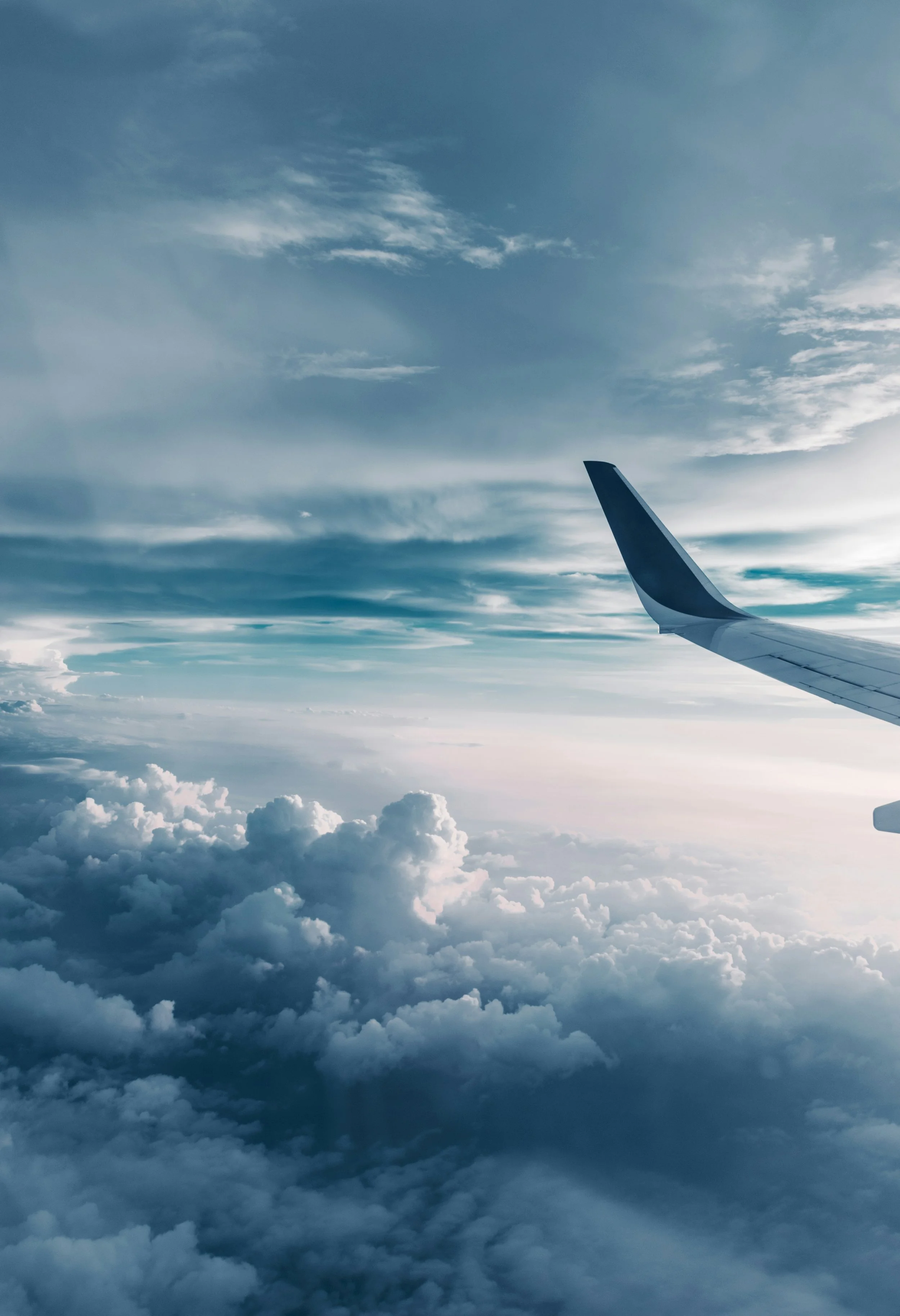 A view from an airplane window showing part of the airplane's wing and a sky filled with clouds and blue sky.