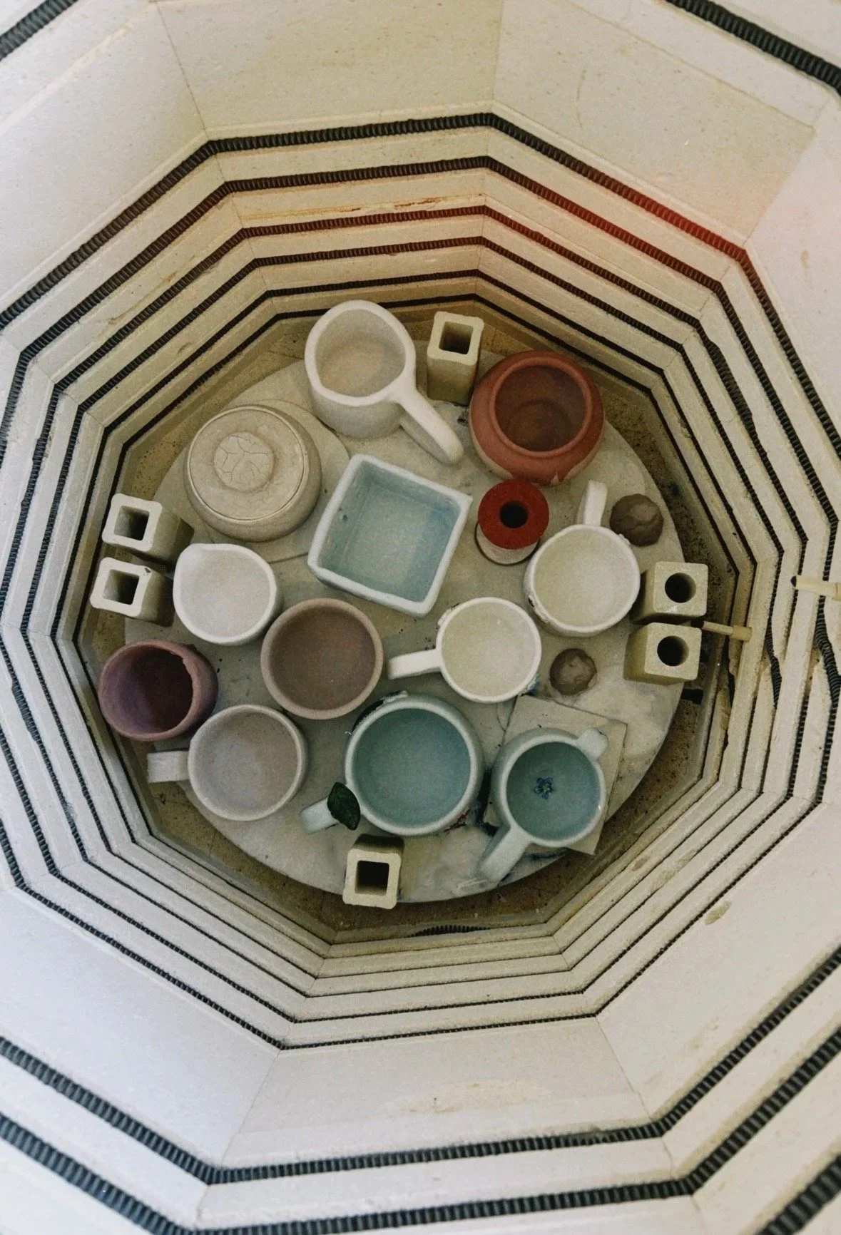 Arrangement of various ceramic cups and containers inside a decorative tiled wall encasement.