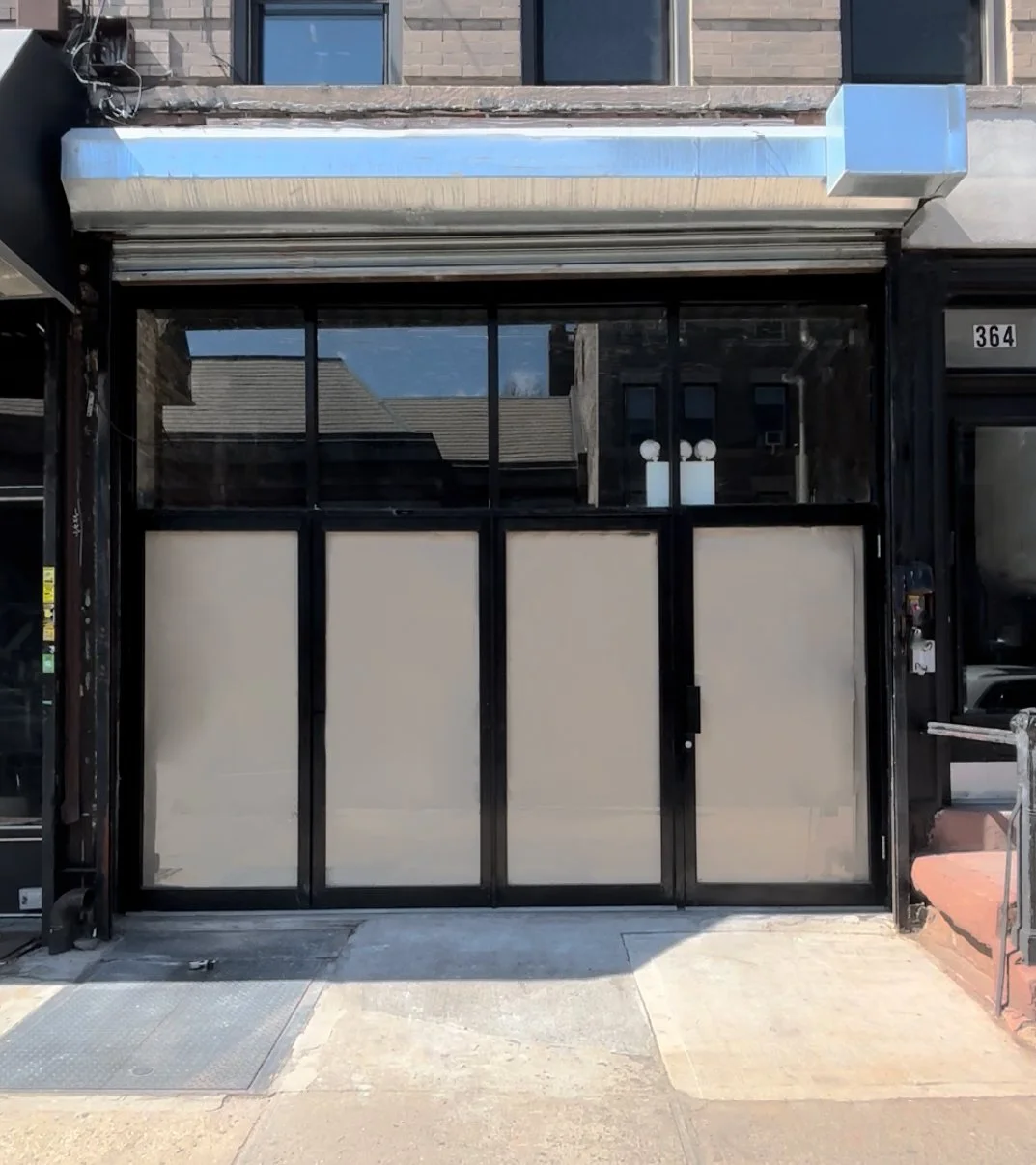 Closed storefront with sliding glass doors and black frames, glass windows above, and a metallic blue and silver awning.