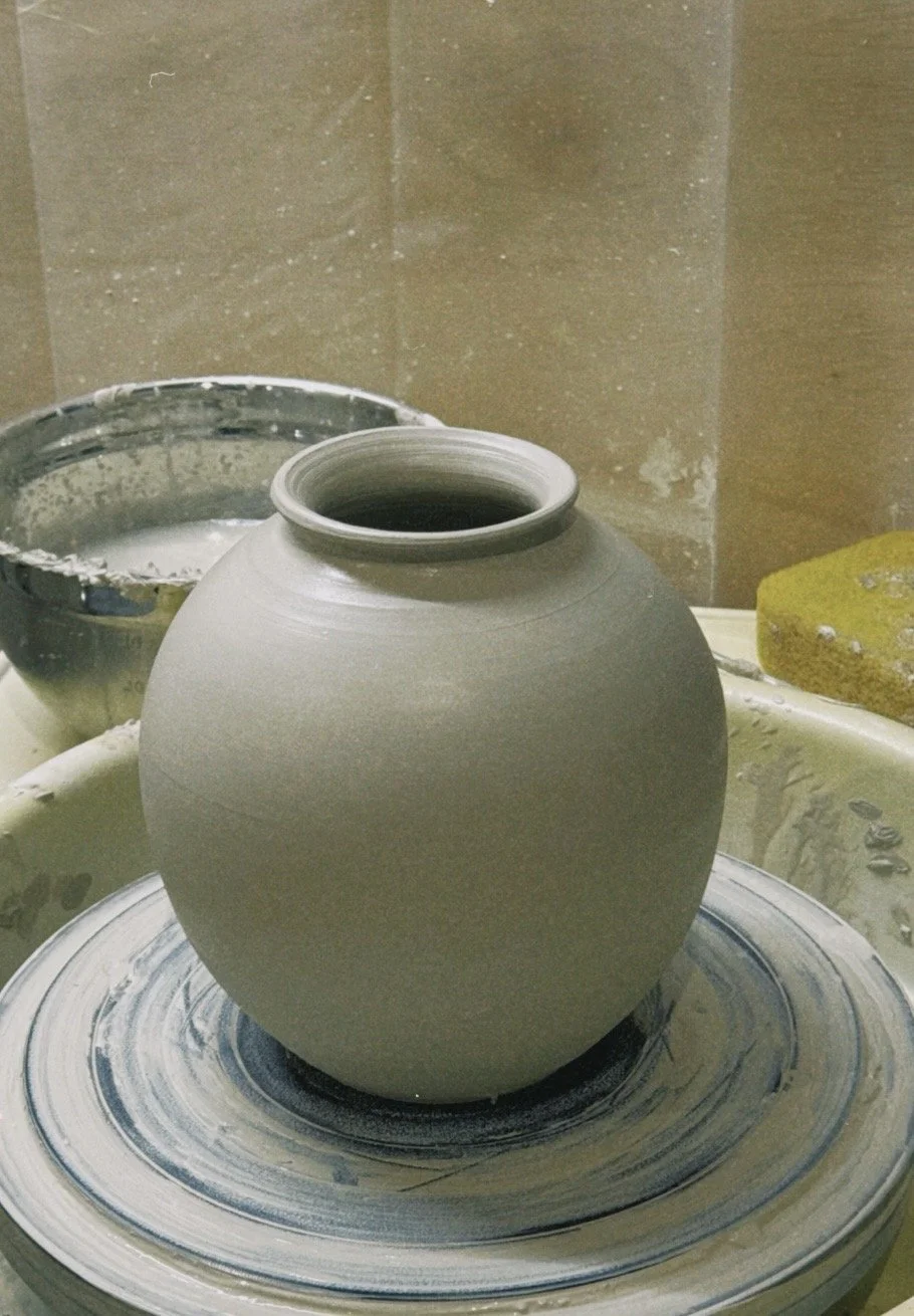 A ceramic vase in progress on a pottery wheel in a pottery studio.