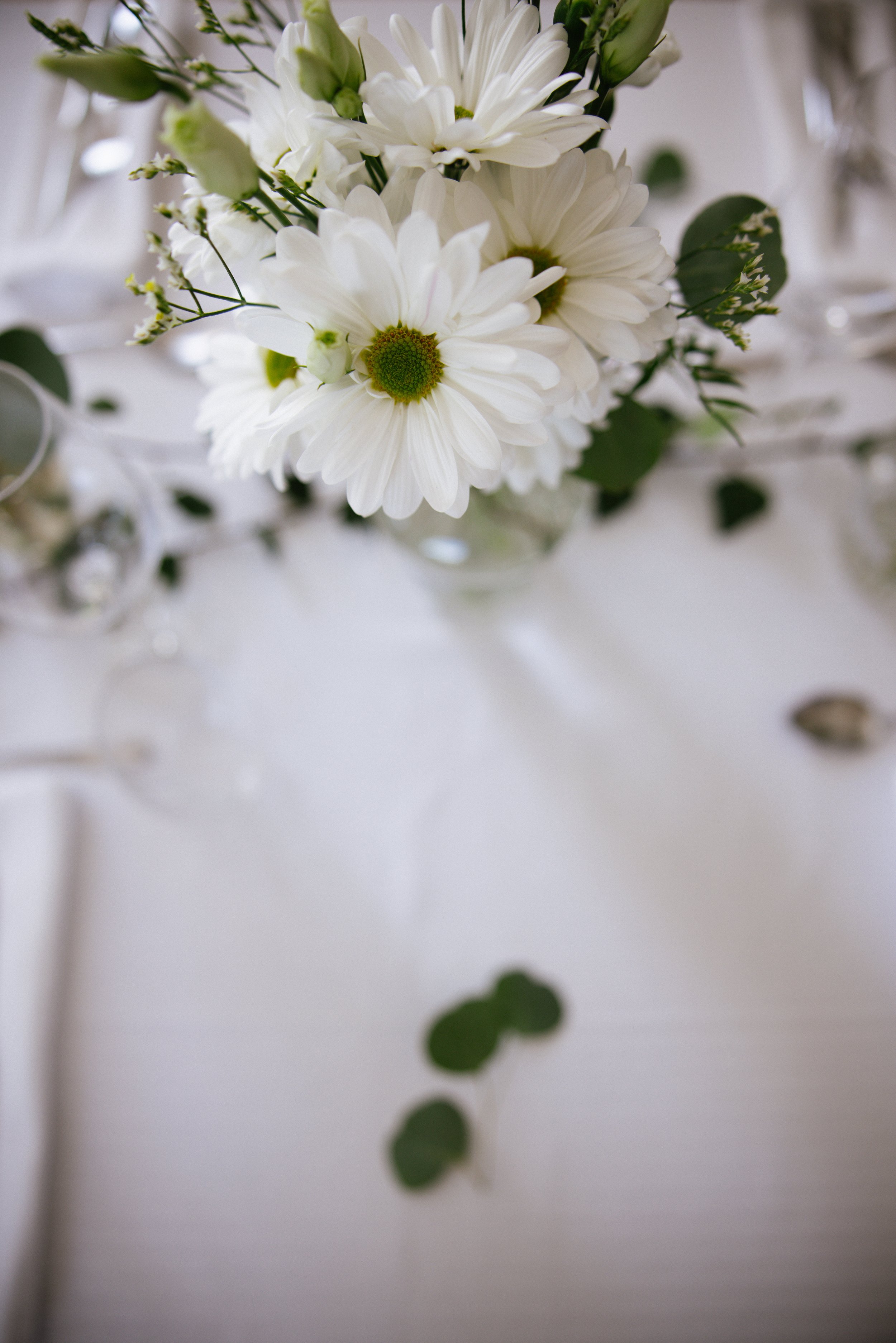 Un bouquet de fleurs blanches, principalement des marguerites, placé sur une table blanche.