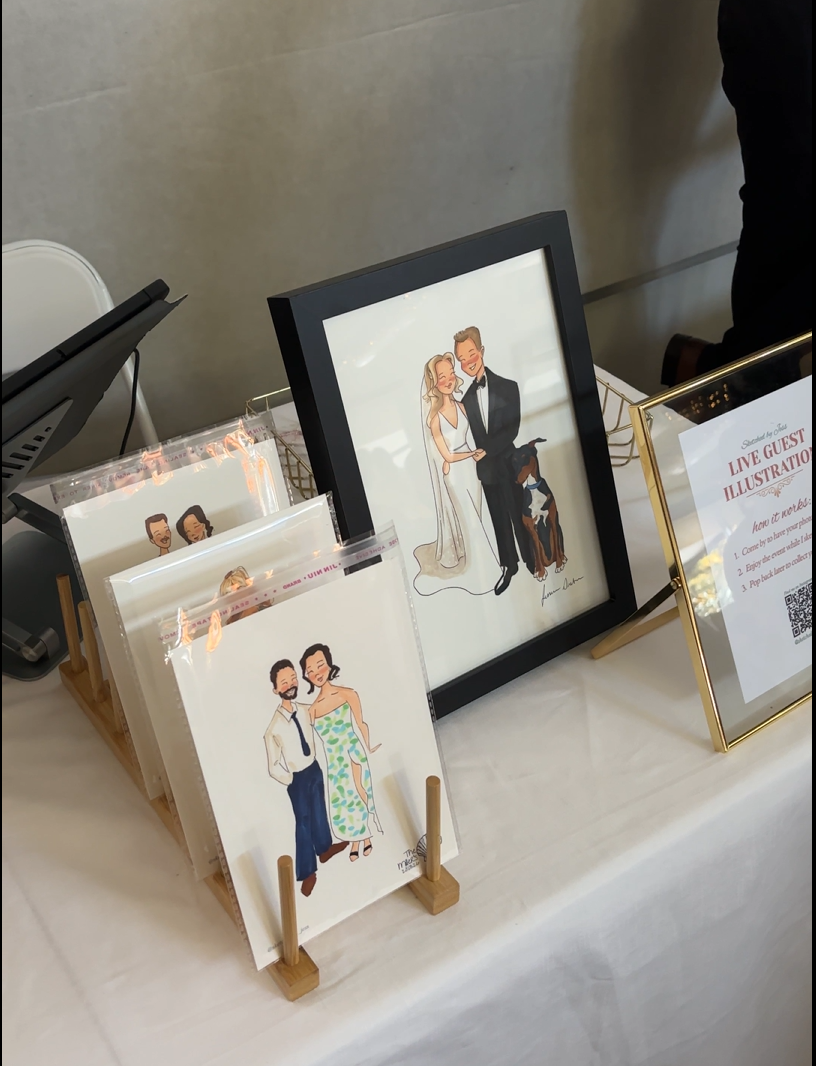Picture depicts table display at wedding. Guest portraits displayed in holder. Wedding couple portrait in frame and sign with the words live illustration.