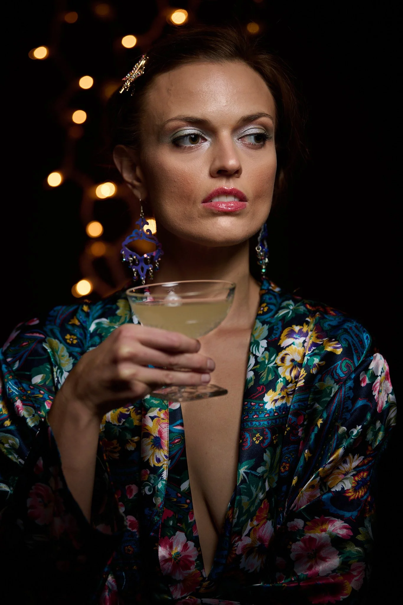 Model Whitney Holcombe during cocktail hour - wearing a colorful floral silk robe, holding a mixed drink, and backed by sultry bokeh lighting