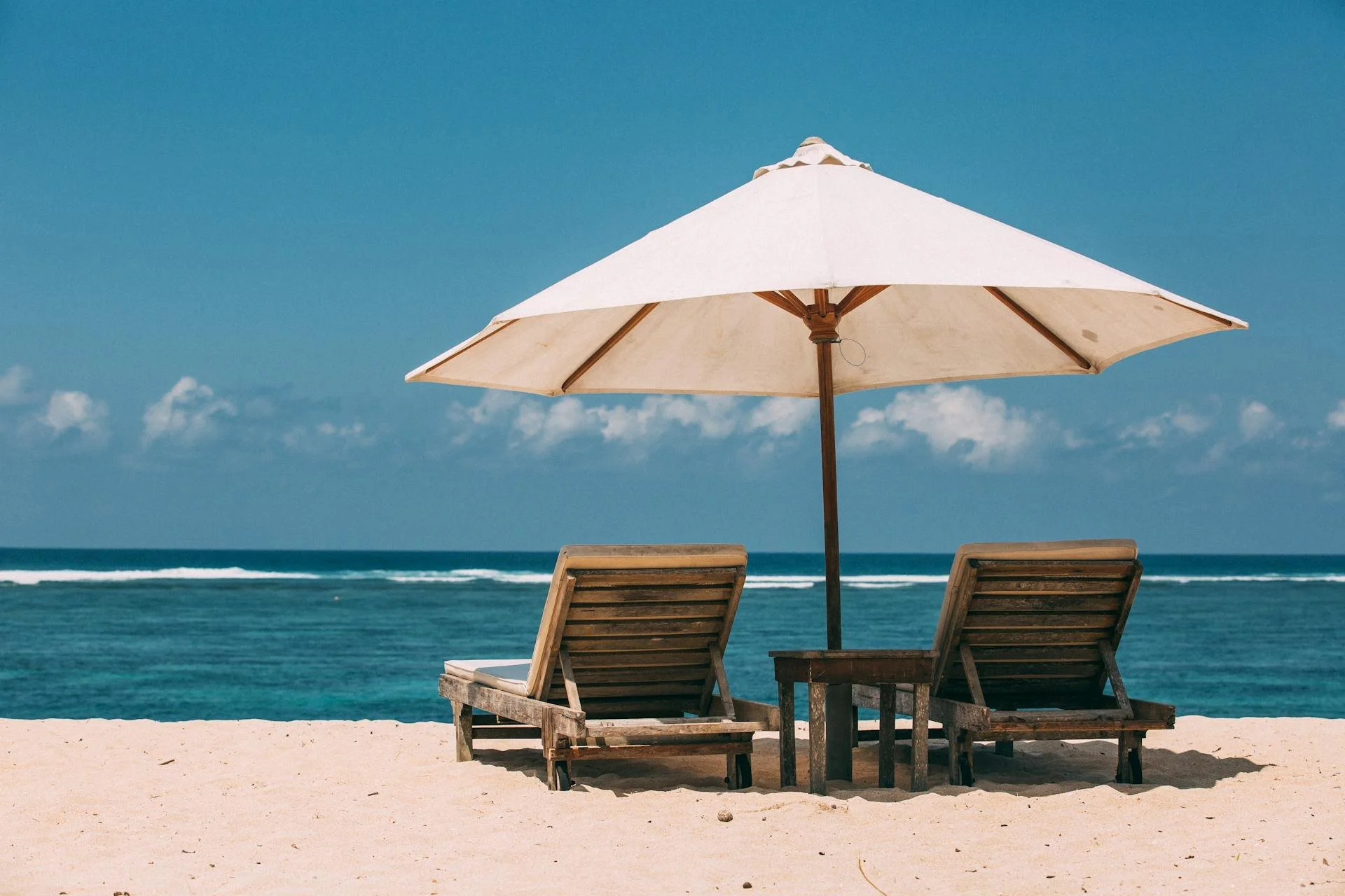 two lounge chairs under an umbrella on the beach