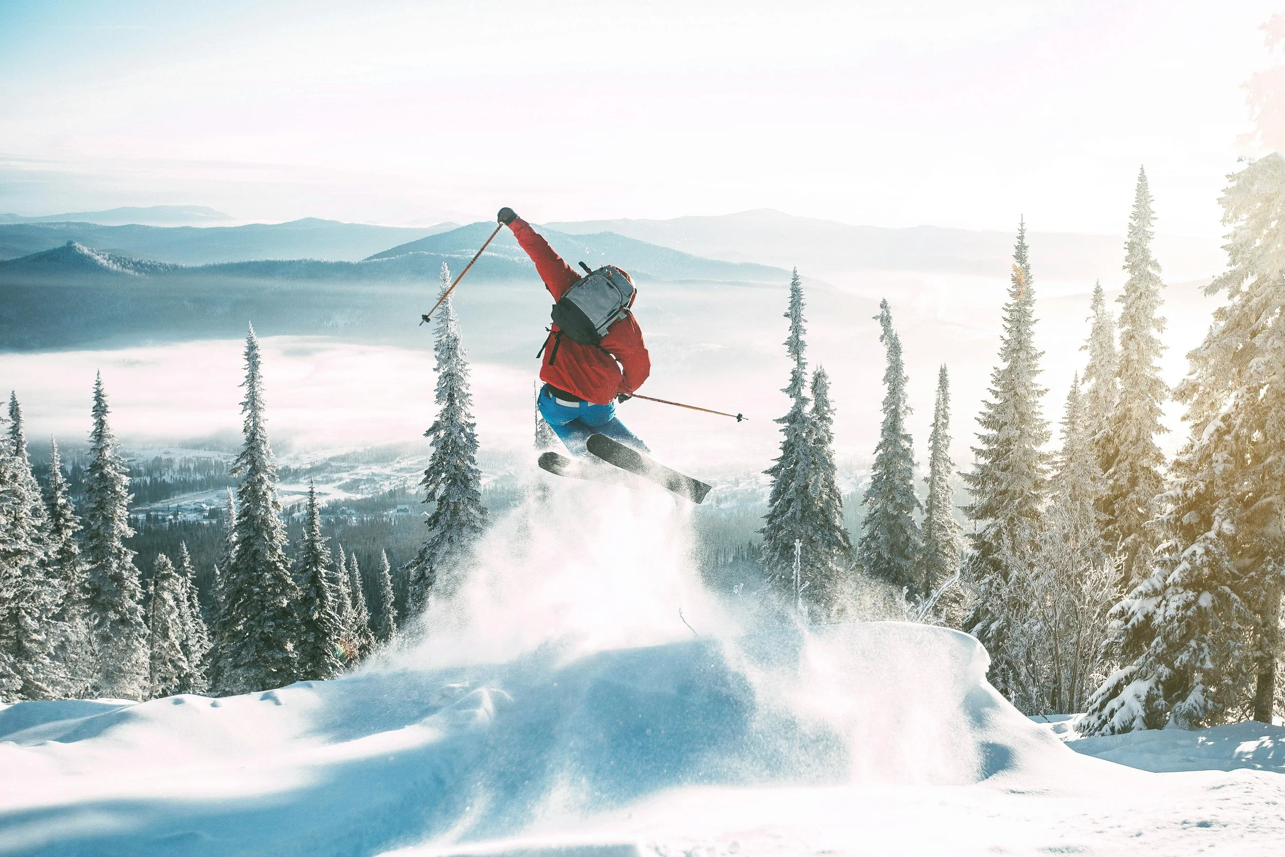 A skier going off a jump looking over the valley below