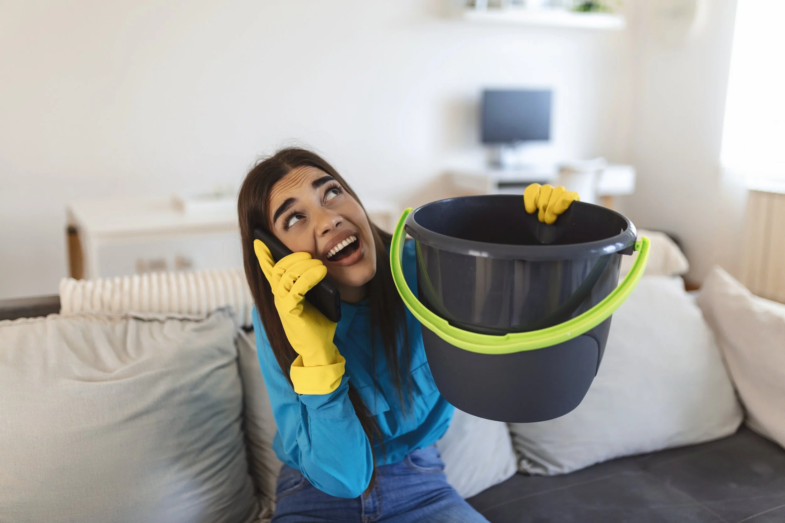 A shocked woman holding a bucket catching leaking water