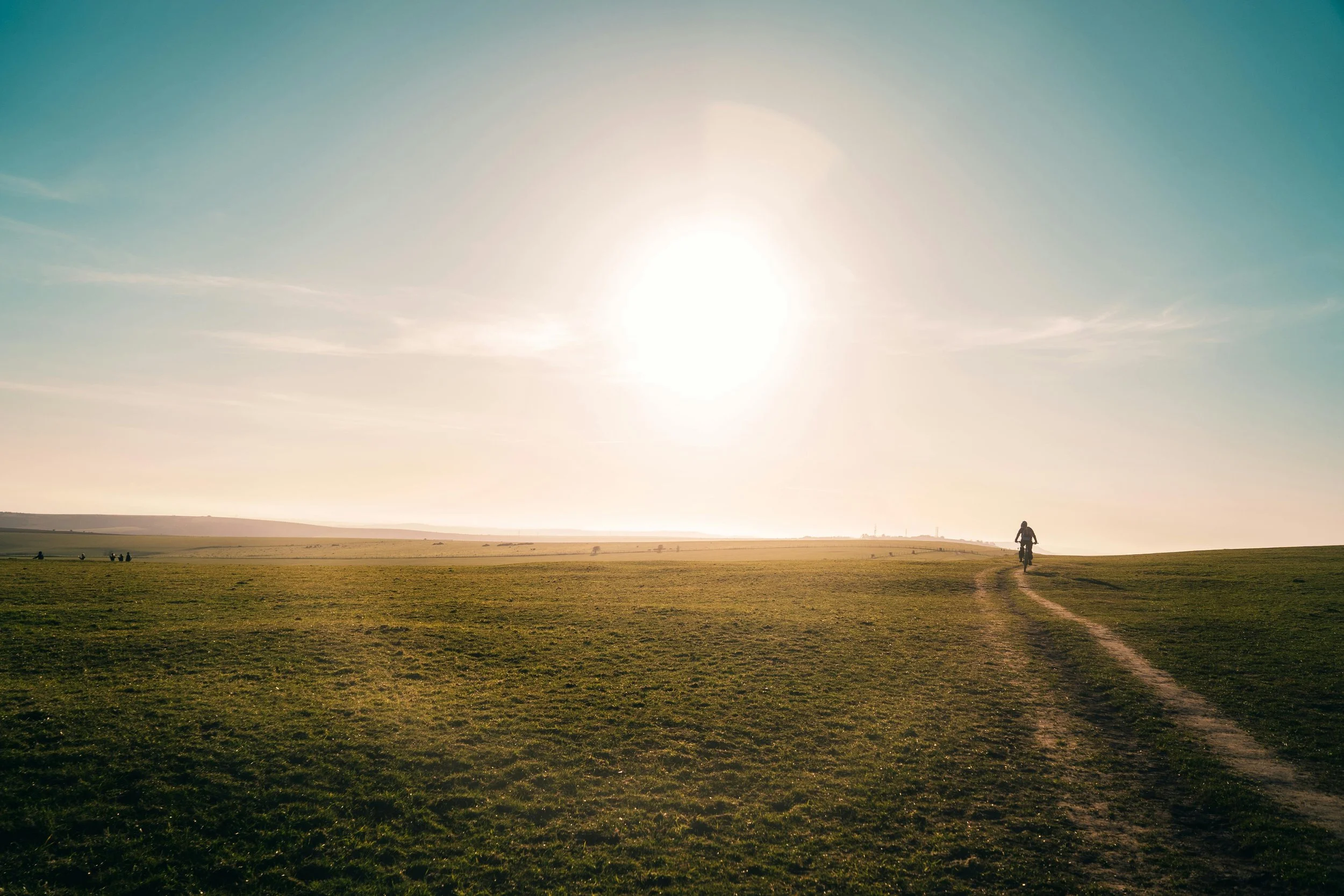 person riding their bike along a country path toward the sun