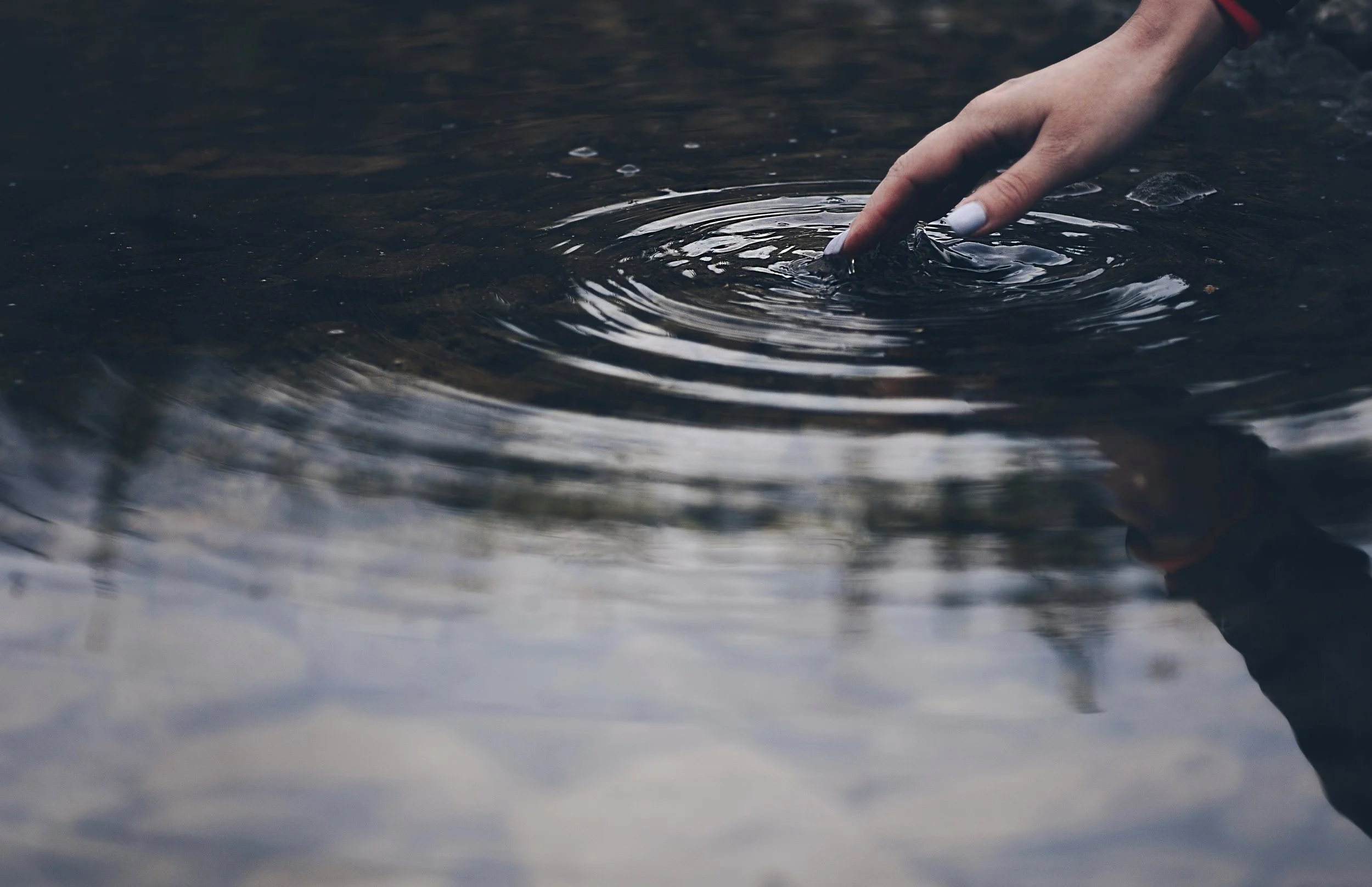 a finger creating ripples across the water