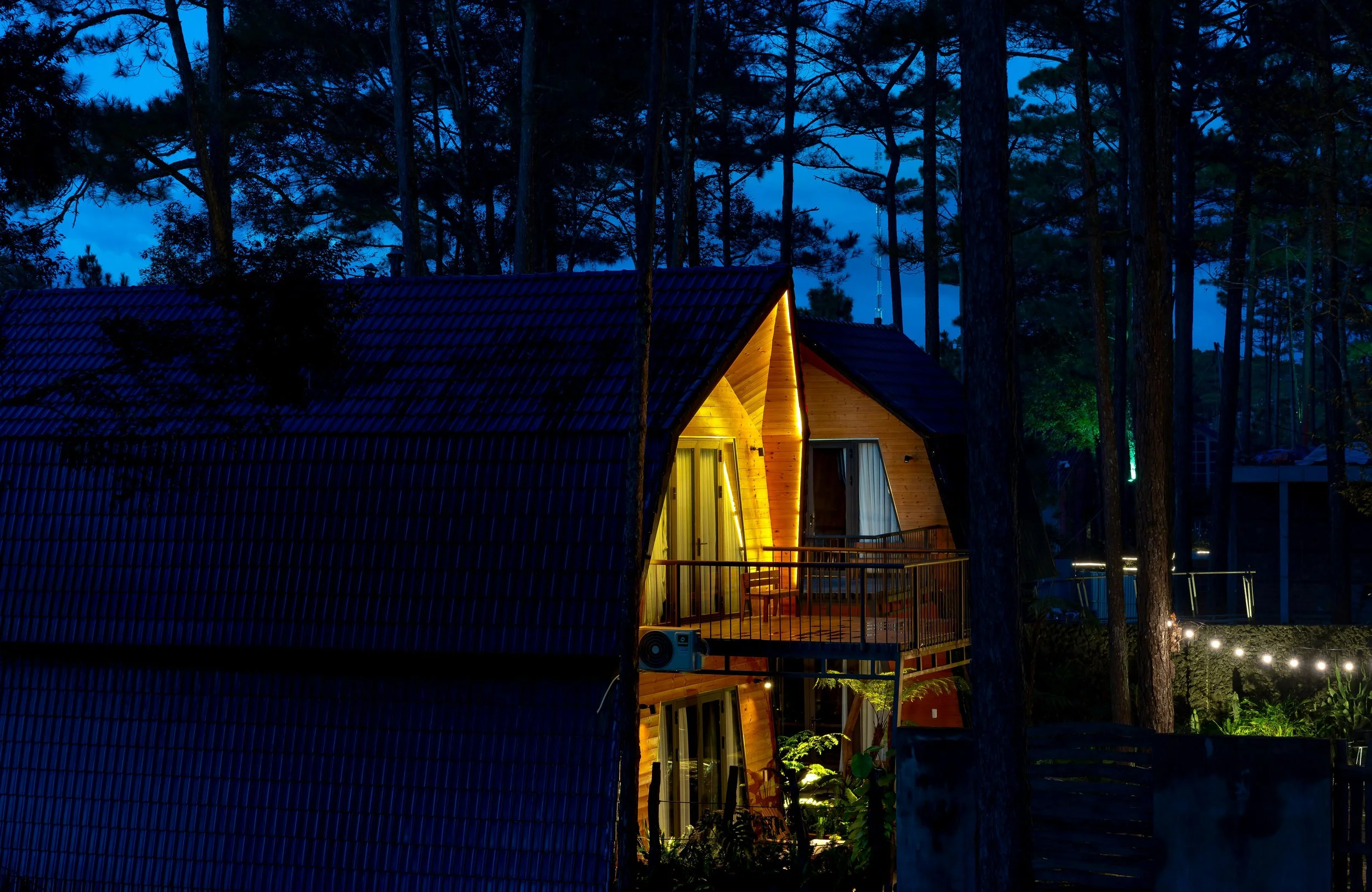 Warmly lit cabin at dusk in a pine forest, with dark blue sky and trees.”