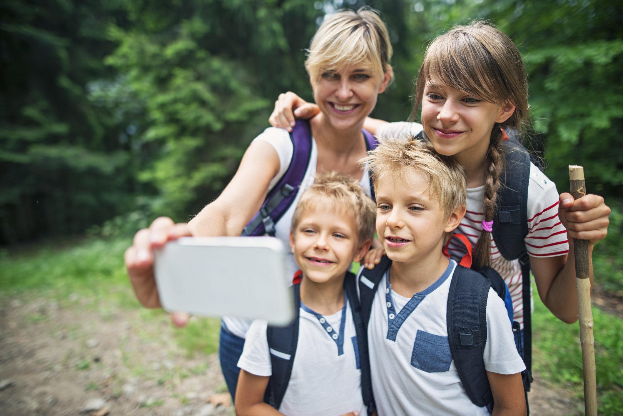 A woman and four children taking a selfie outdoors in a forest with green trees.