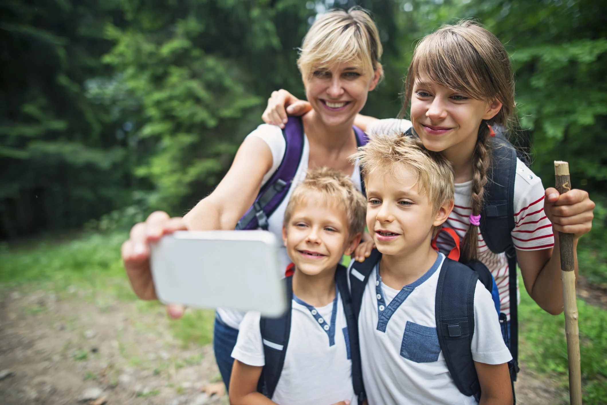 A woman with three children taking a selfie with a smartphone during a hike in the woods.