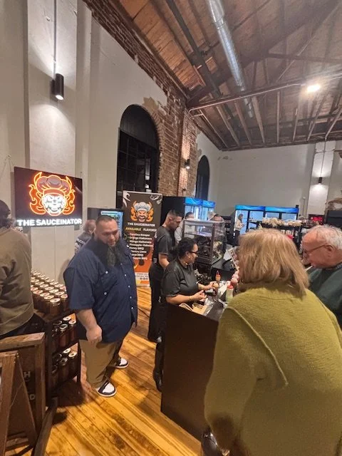 People ordering food at a restaurant counter with a sign displaying the logo 'The Sauceinator' and a poster showing menu options