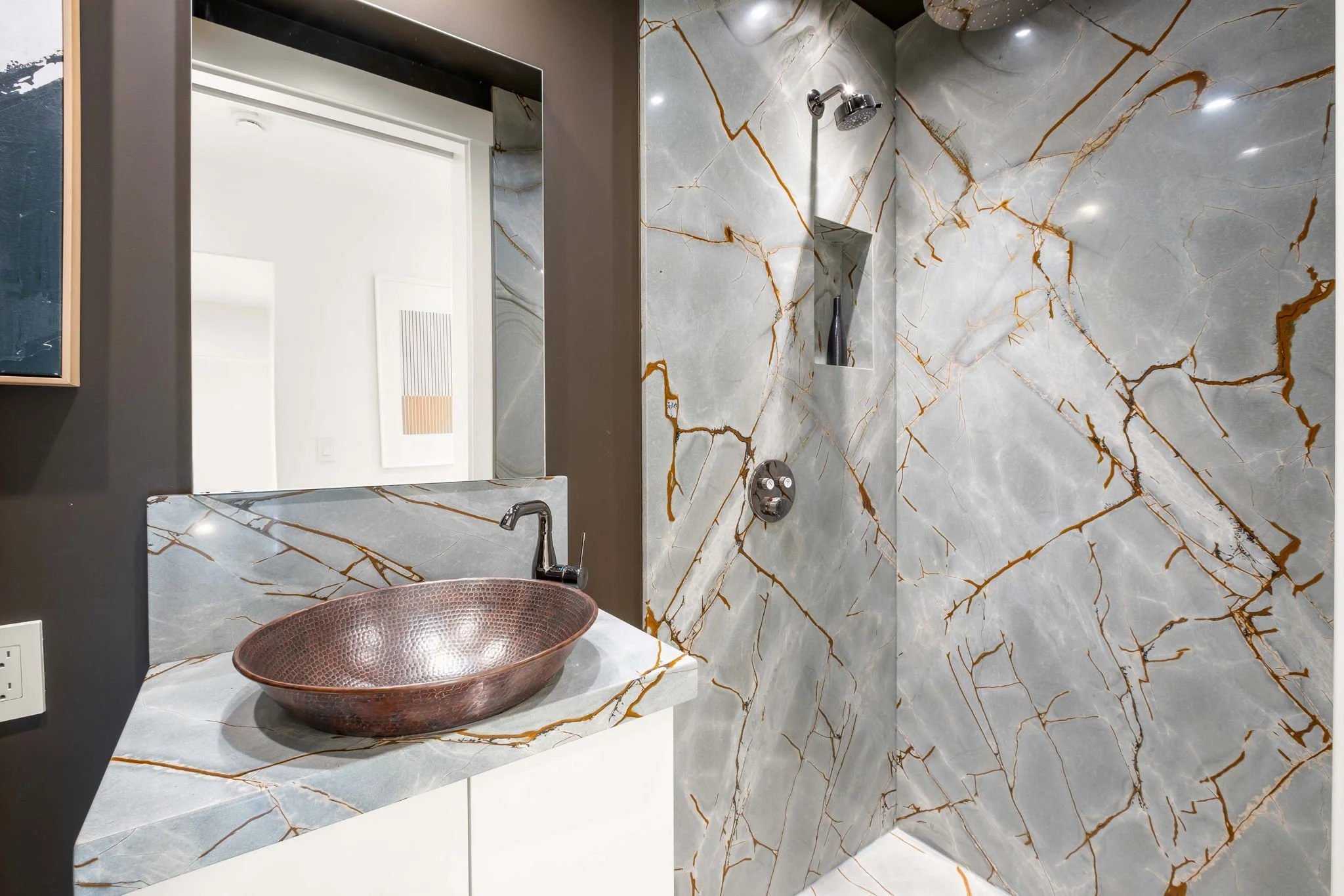 Modern bathroom with marble walls and countertop, a copper sink, and a wall-mounted showerhead.