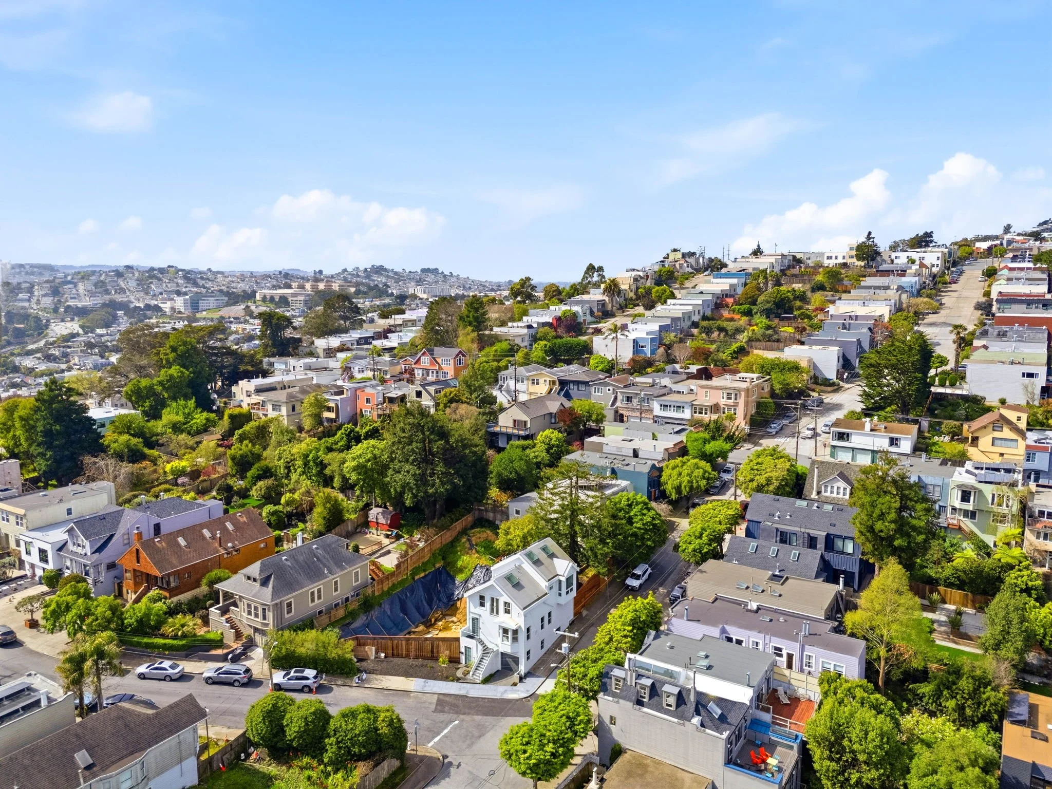 Aerial view of a hillside residential neighborhood with houses and trees under a blue sky.