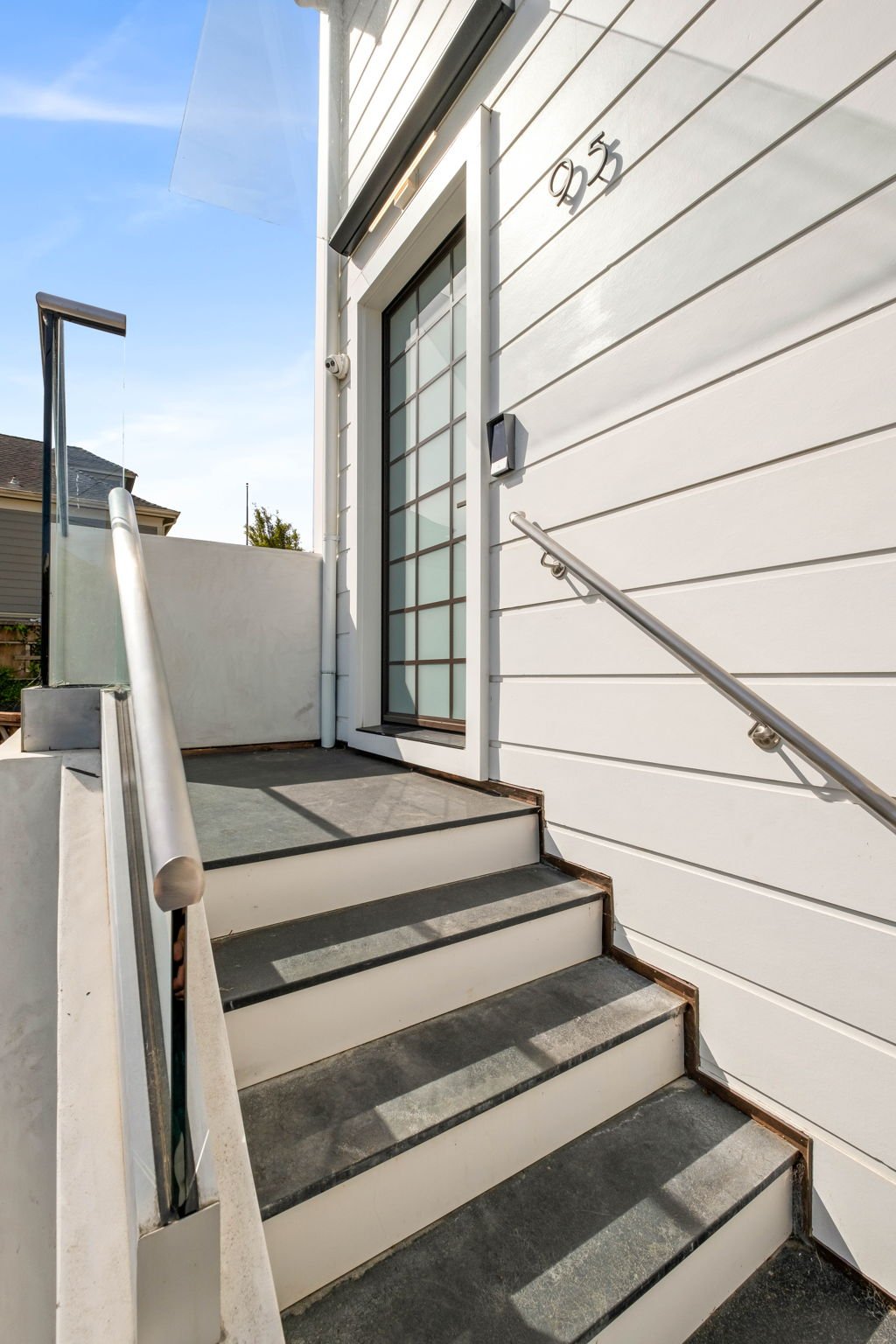 Exterior view of a house entrance with a small staircase, glass sliding door, and white siding wall, under a clear sky.