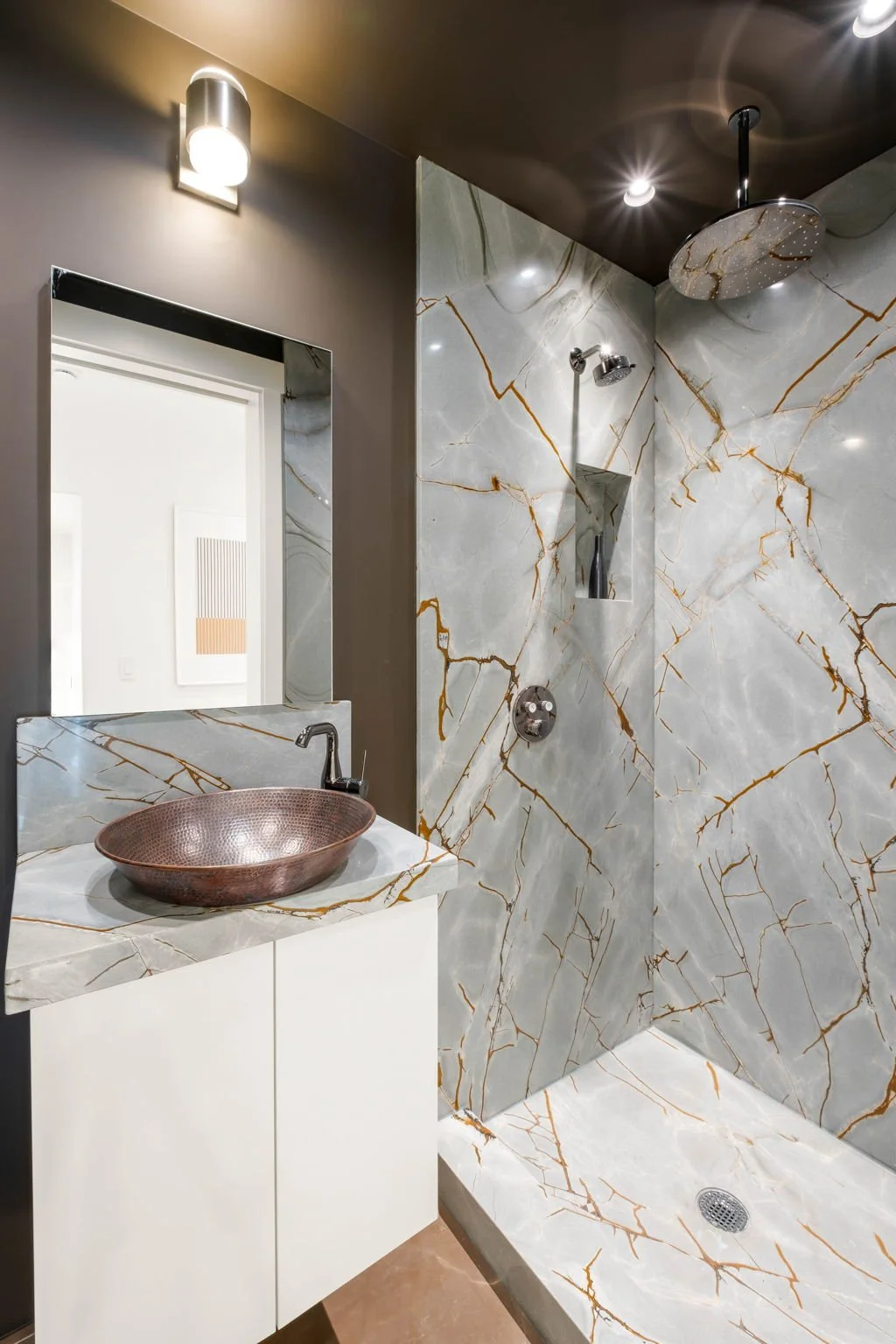 Modern bathroom with marble walls, a copper vessel sink, a mirror, and a shower with a rainfall showerhead.